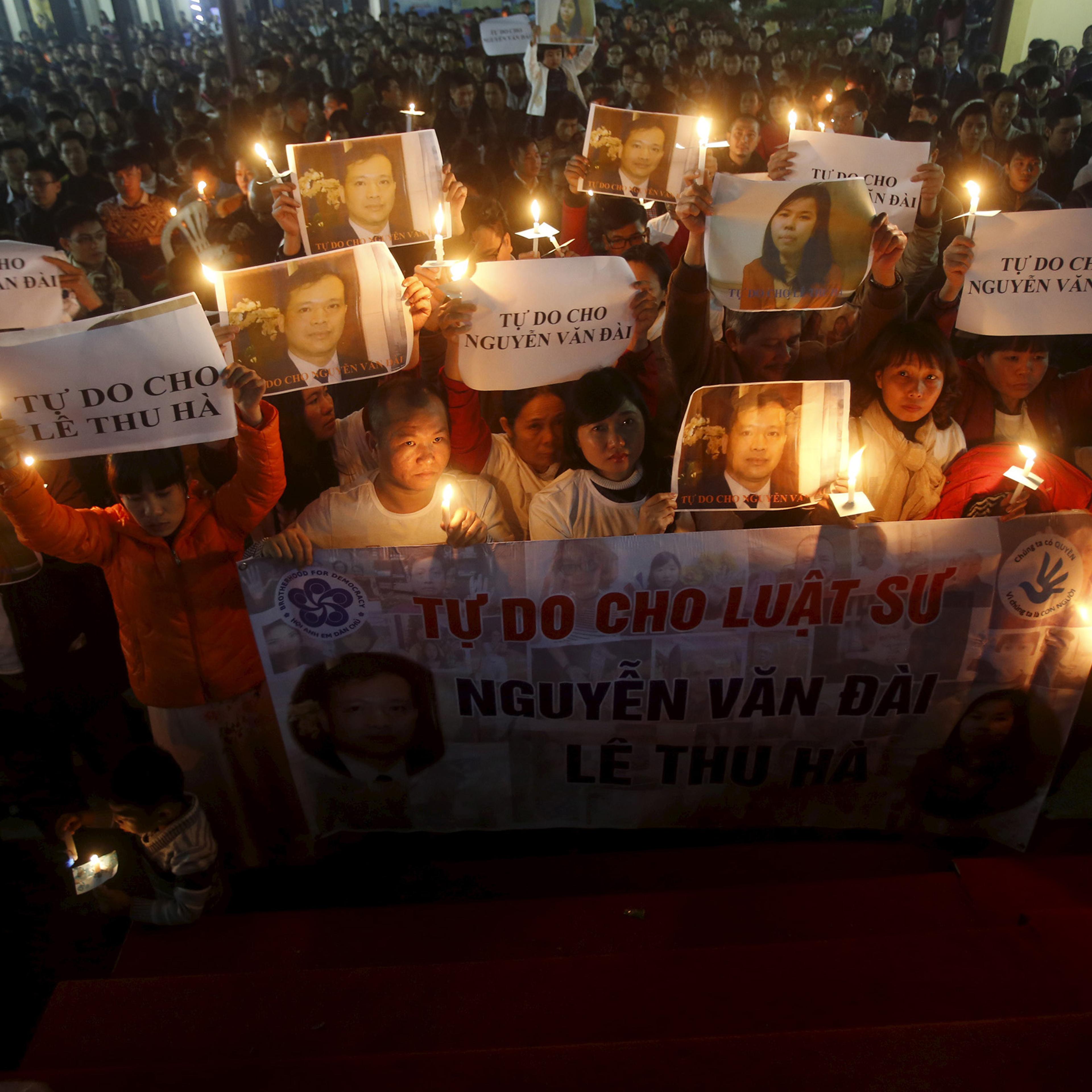Vu Minh Khanh holds an image of her husband Nguyen Van Dai as Catholics hold candles and image of Dai's assistant Le Thu Ha during a mass prayer for Dai and Ha at Thai Ha church in Hanoi, Dec. 27, 2015.