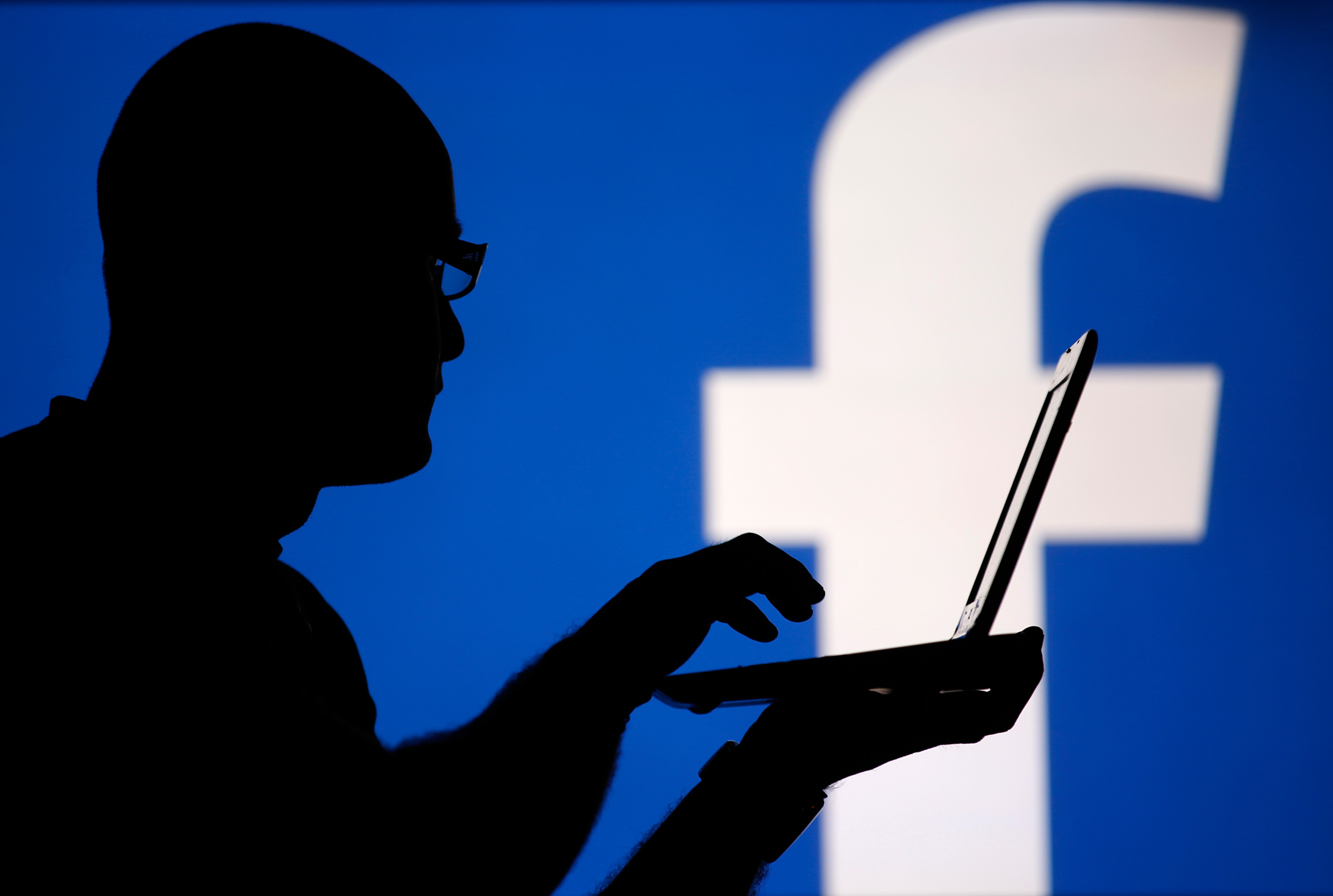 A man is silhouetted against a video screen with an Facebook logo as he poses with an Dell laptop in this photo illustration taken in the central Bosnian town of Zenica, August 14, 2013. REUTERS/Dado Ruvic (BOSNIA AND HERZEGOVINA - Tags: BUSINESS TELECOM