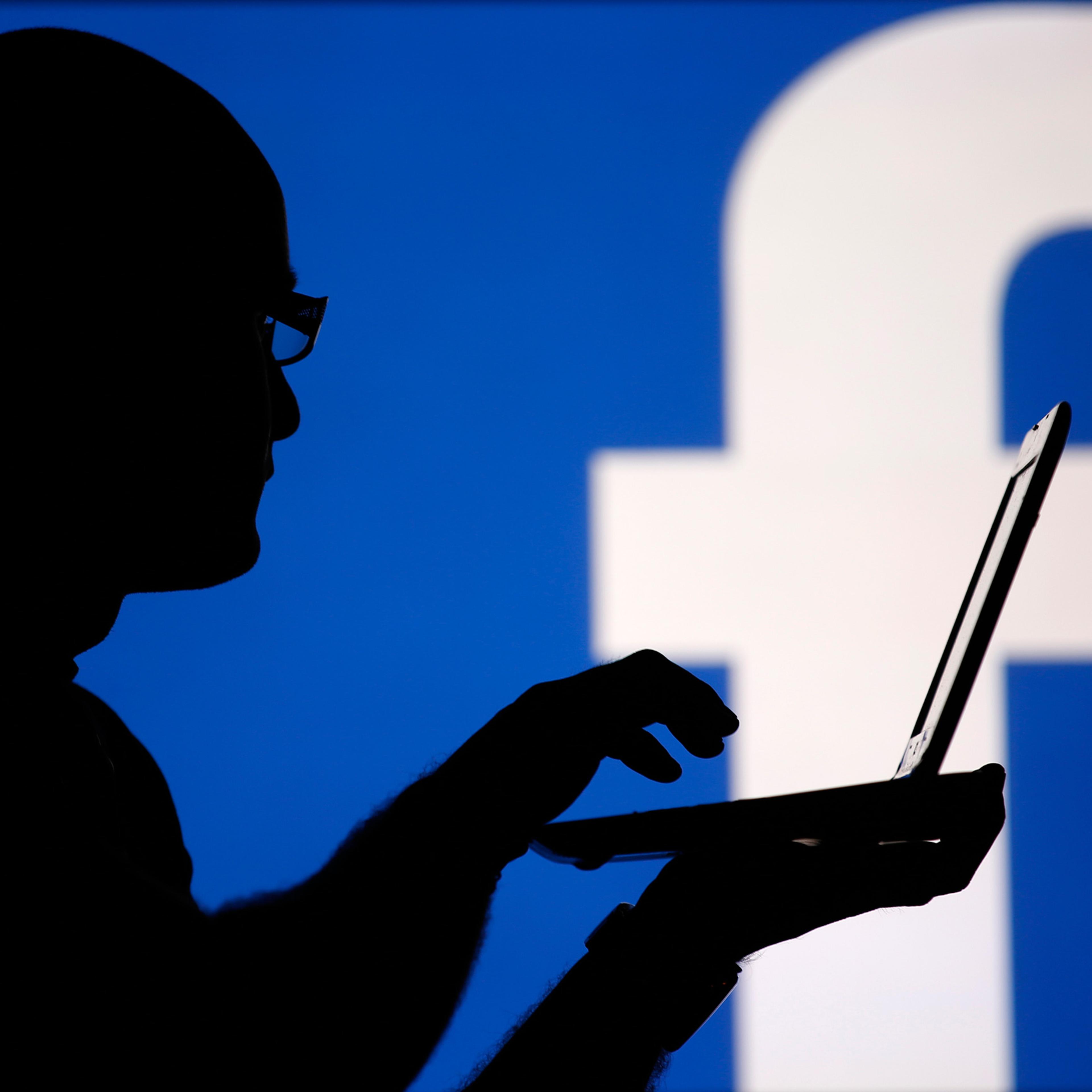 A man is silhouetted against a video screen with an Facebook logo as he poses with an Dell laptop in this photo illustration taken in the central Bosnian town of Zenica, August 14, 2013. REUTERS/Dado Ruvic (BOSNIA AND HERZEGOVINA - Tags: BUSINESS TELECOM