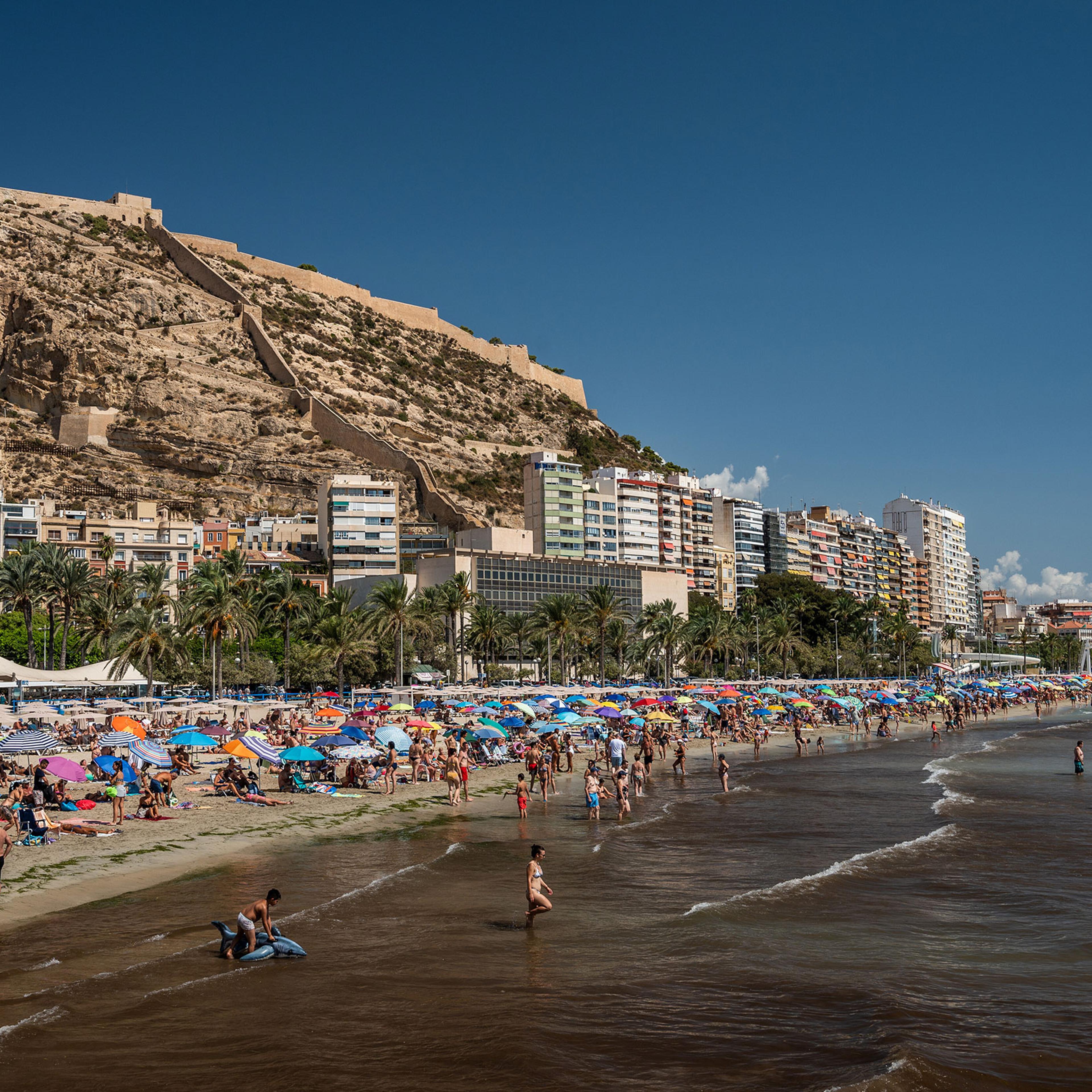 Tourists and locals crowd El Postiguet Beach on a hot August day in Alicante, Spain.