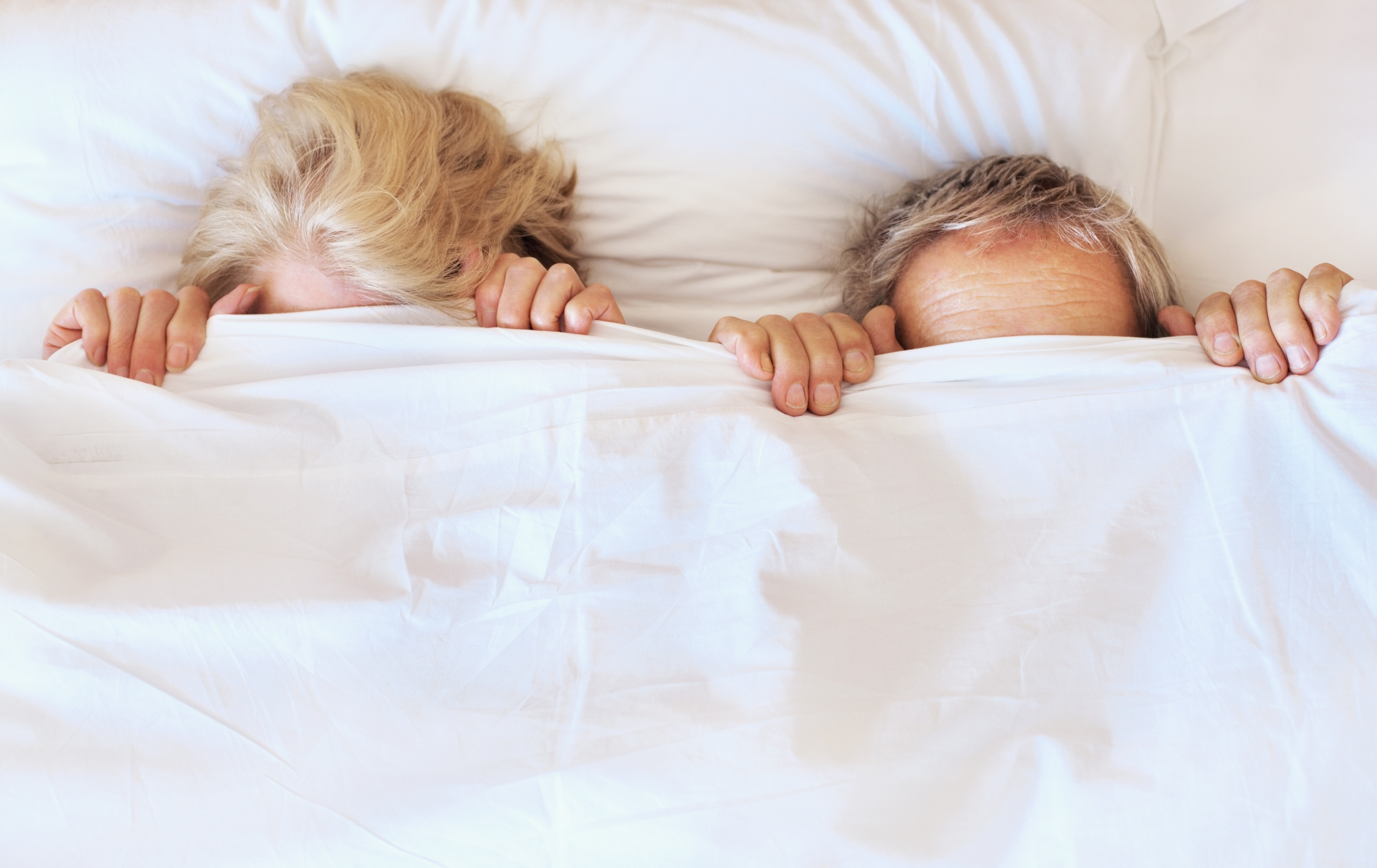 Couple in bed with a bedsheet covering faces TIME health stock