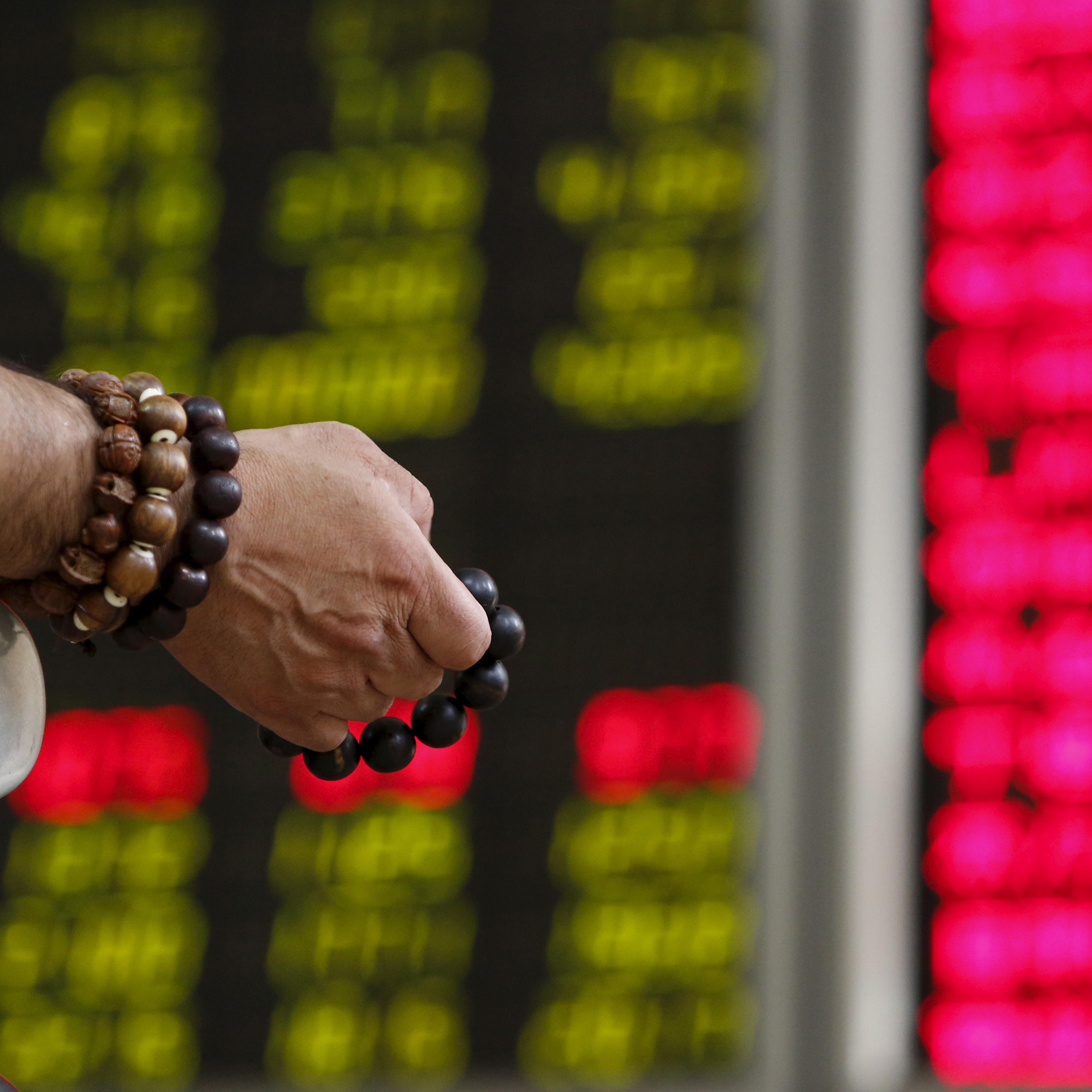 An investor holds onto prayer beads as he watches a board showing stock prices at a brokerage office in Beijing