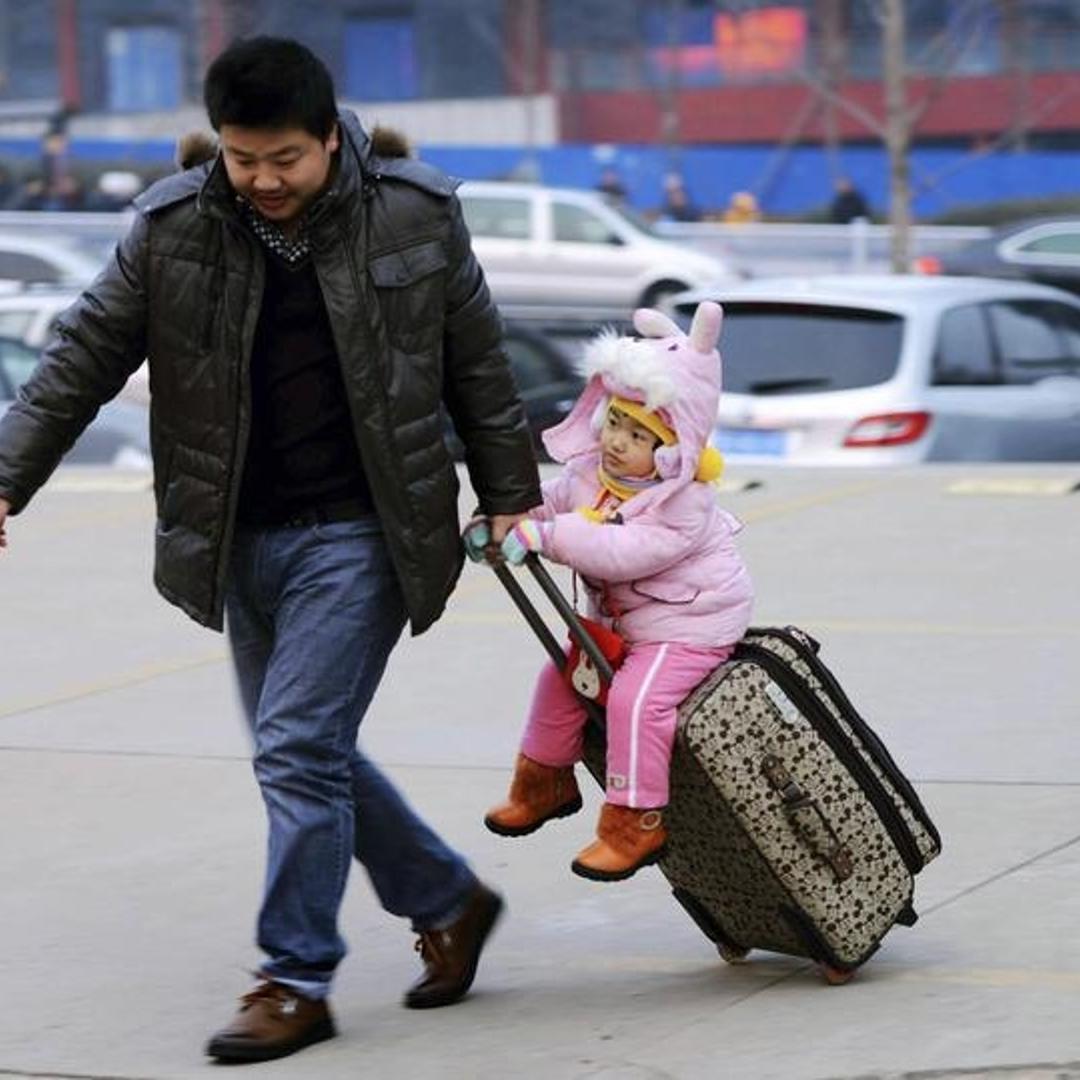 A man drags a suitcase with a girl sitting on it at a long-distance bus terminus in Qingdao, Shandong province