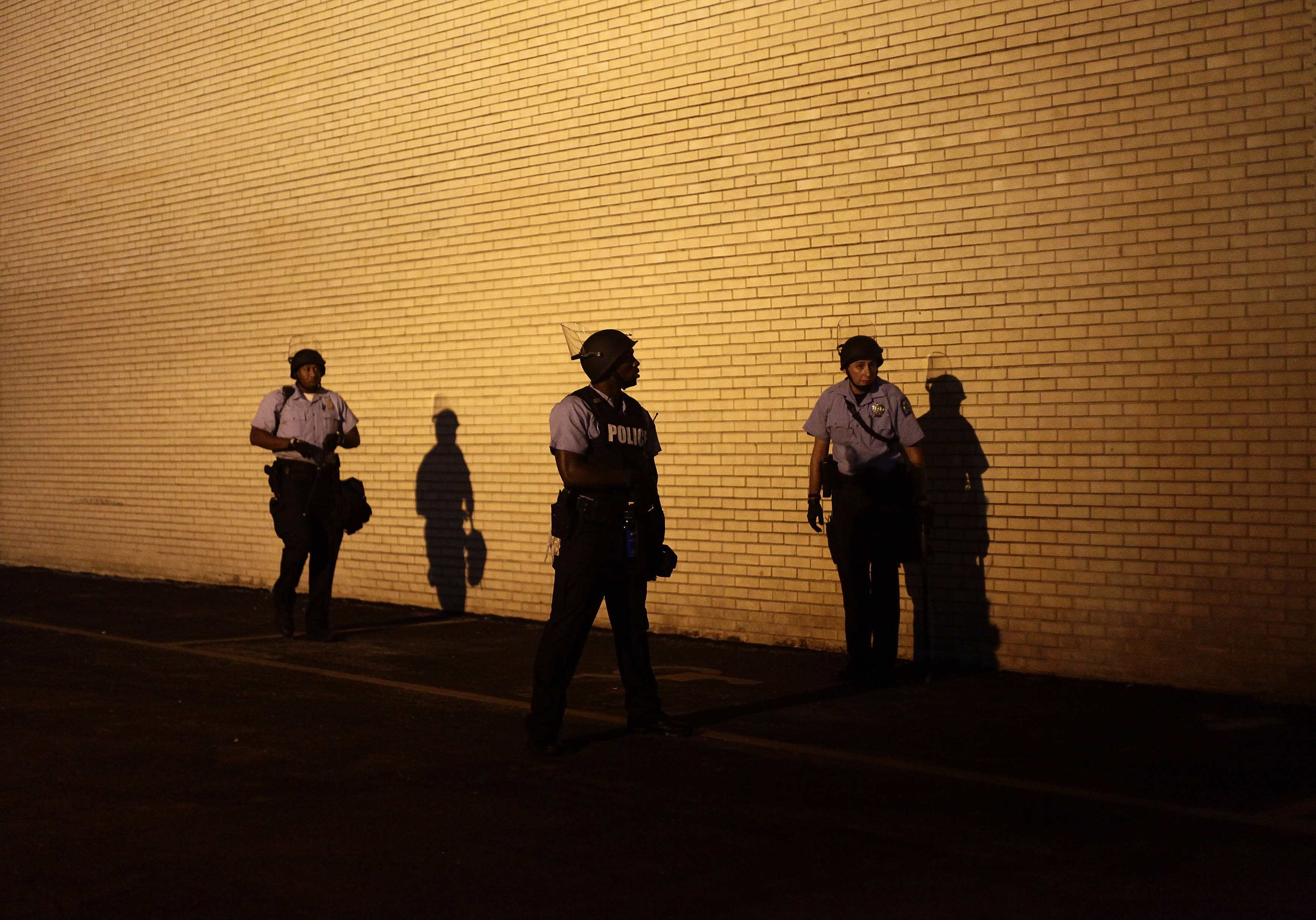 Police officers in riot gear watch demonstrators protesting against the shooting of Michael Brown from the side of a building in Ferguson