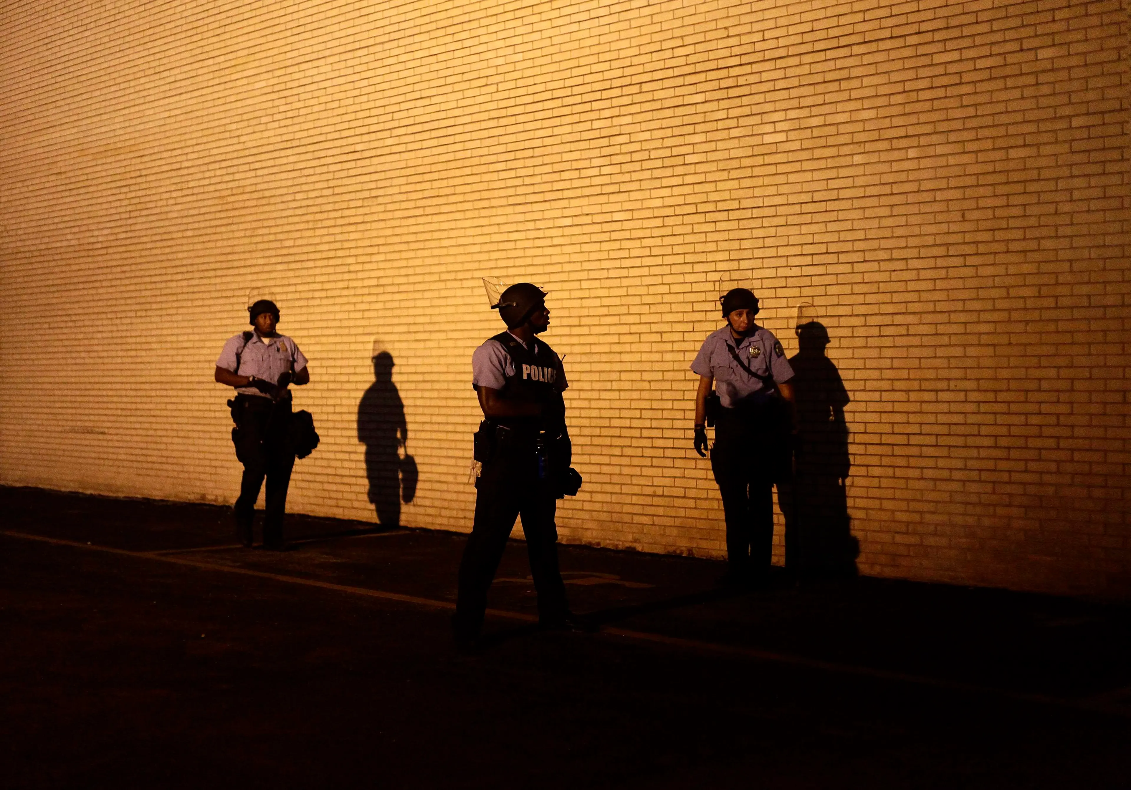 Police officers in riot gear watch demonstrators protesting against the shooting of Michael Brown from the side of a building in Ferguson