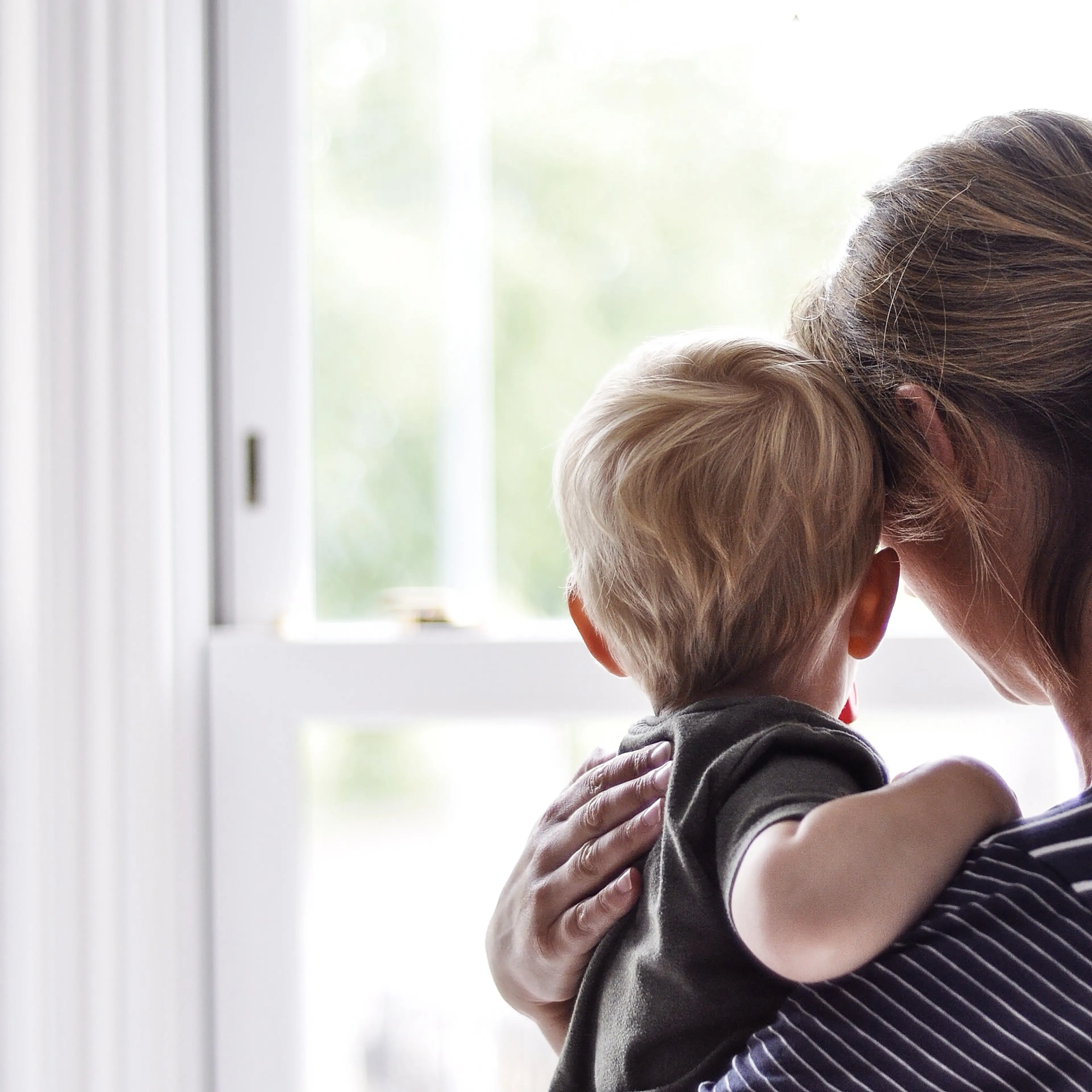 Mother holding son while looking out the window.