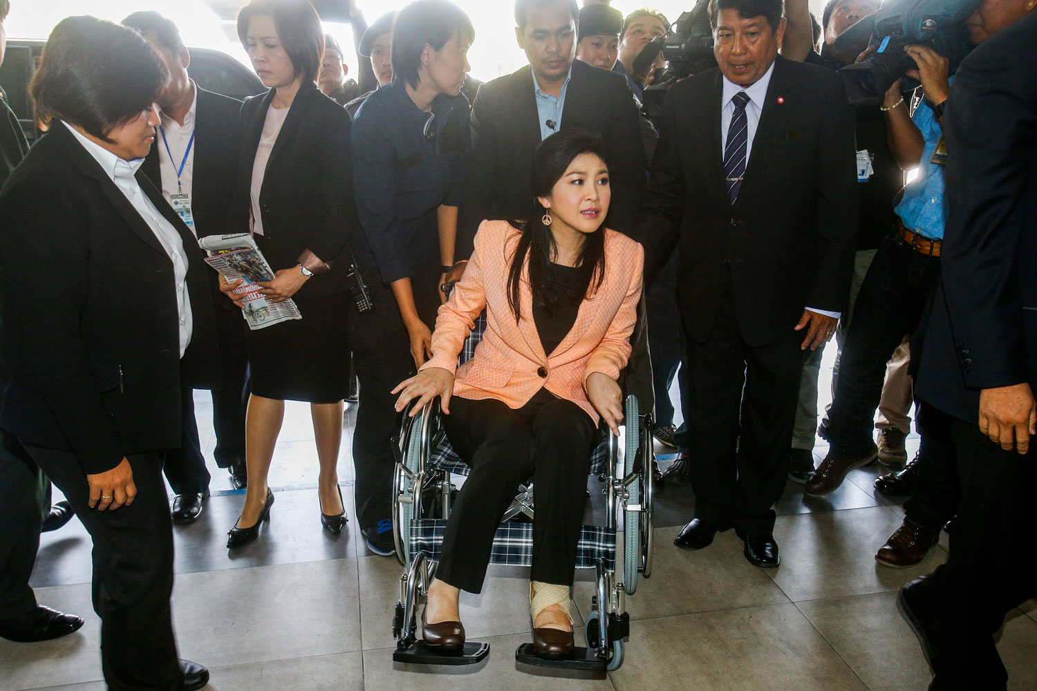 Thailand's Prime Minister Yingluck Shinawatra, center, arrives on a wheelchair at the Royal Police Cadet Academy in Nakorn Pathom province, March 18, 2014.