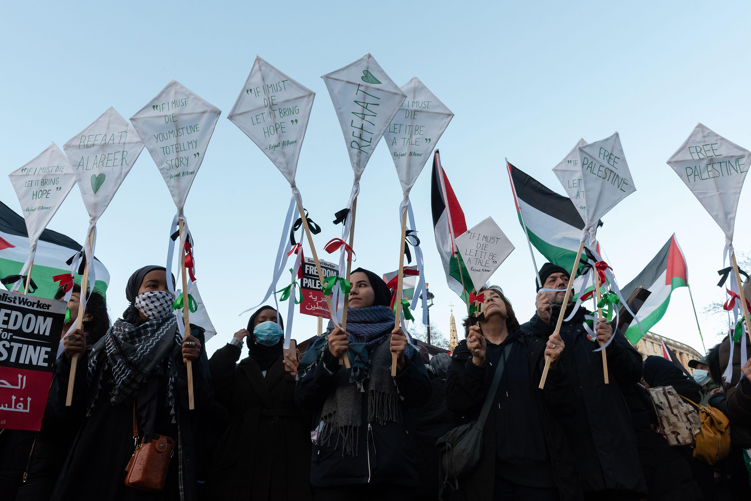 Protesters hold tributes to Palestinian writer, poet, and professor Refaat Alareer, who was killed by an Israeli airstrike, as tens of thousands of Palestine supporters march through central London to Whitehall calling for a permanent ceasefire and an en