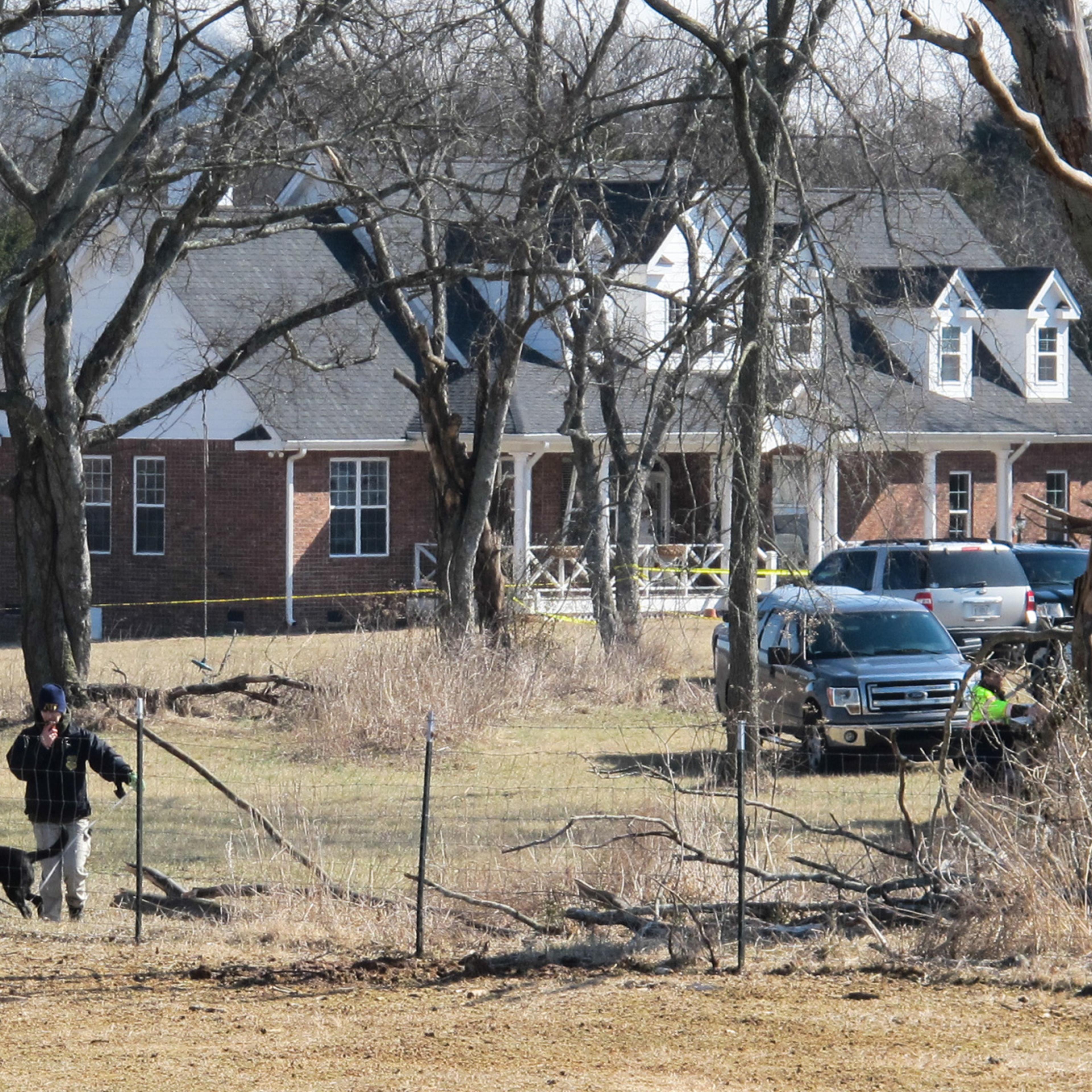 An officer and a dog inspect a fence near a home in Lebanon, Tenn., on Tuesday, Feb. 11, 2014, where police said a package exploded, killing a 74-year-old man and his wife.