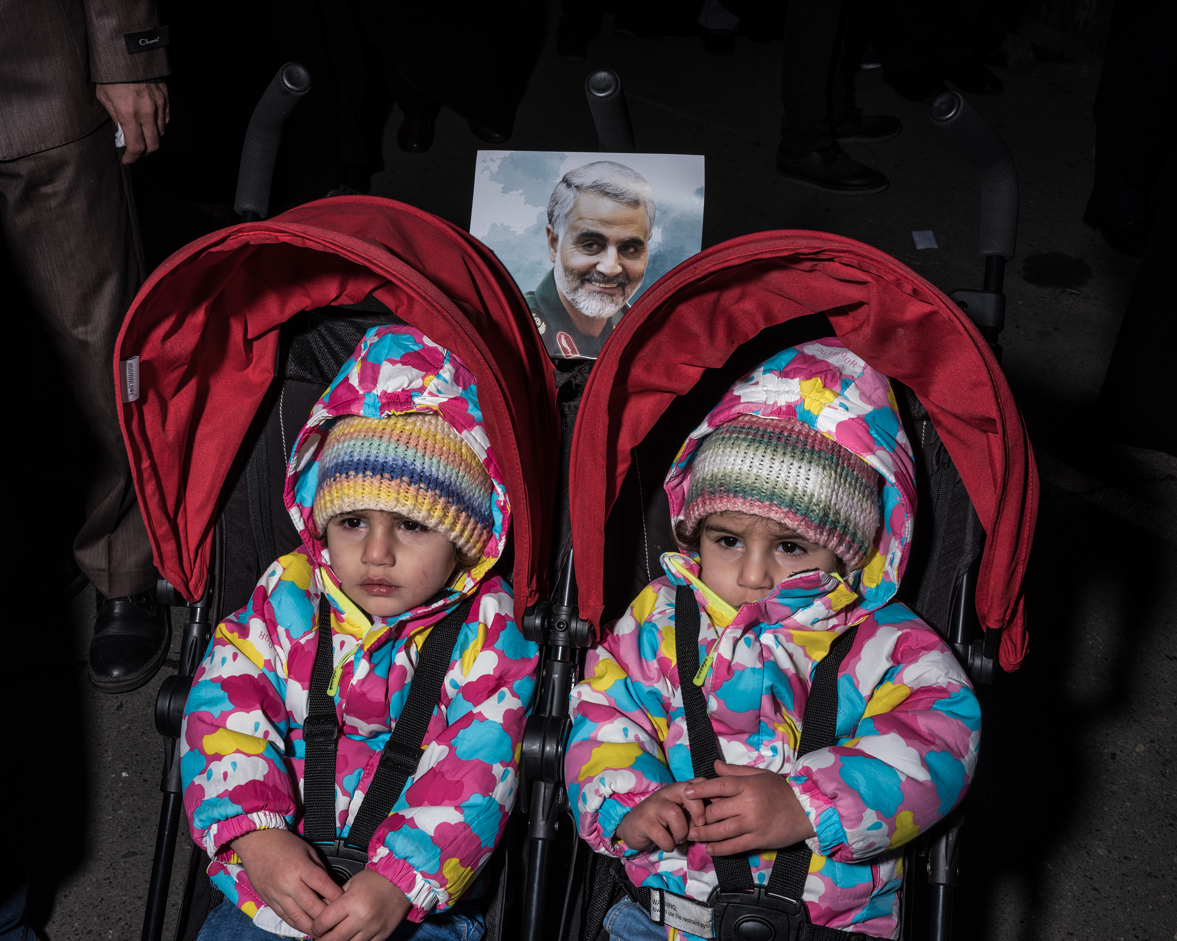 Two girls are pushed in a double stroller in a crowd of mourners.