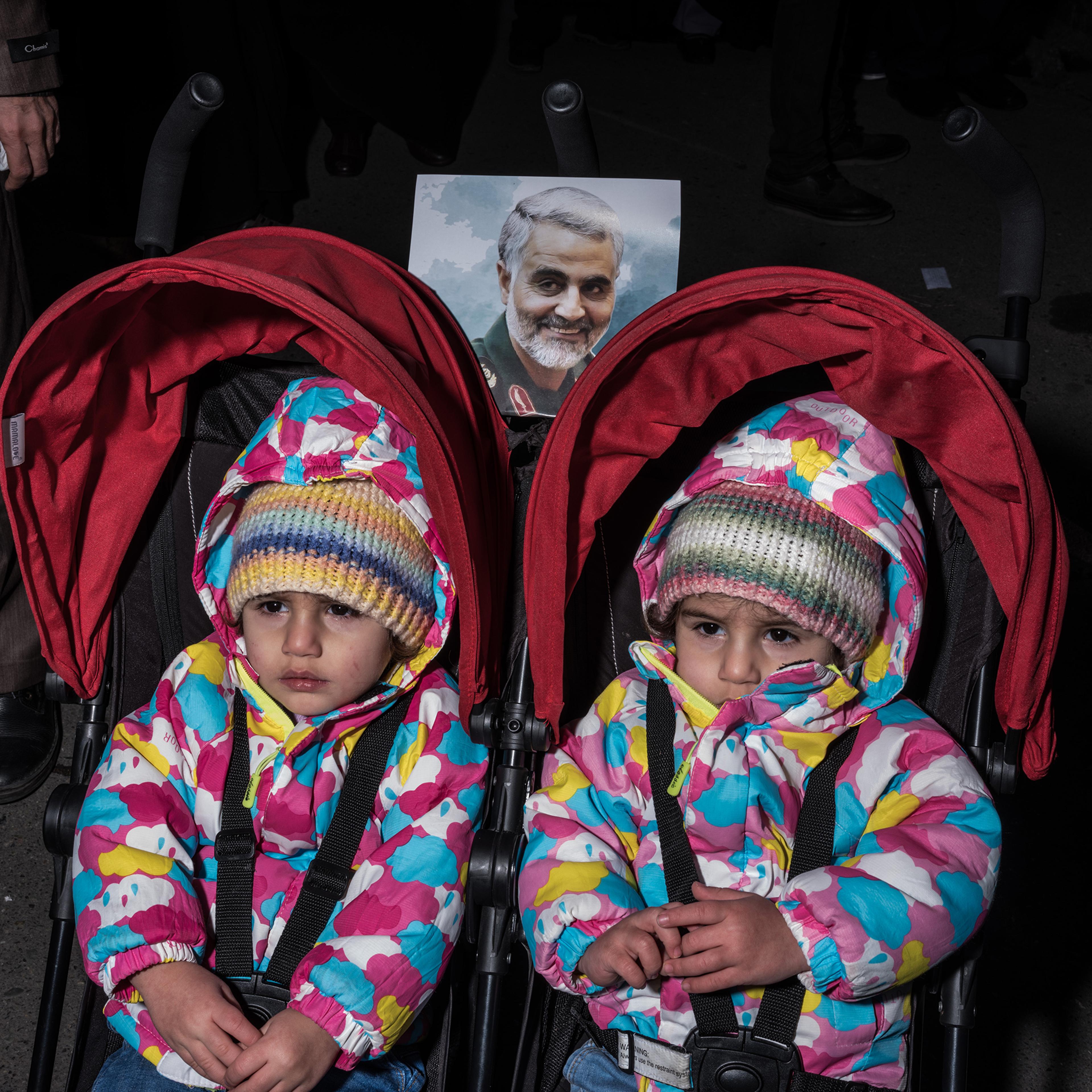 Two girls are pushed in a double stroller in a crowd of mourners.