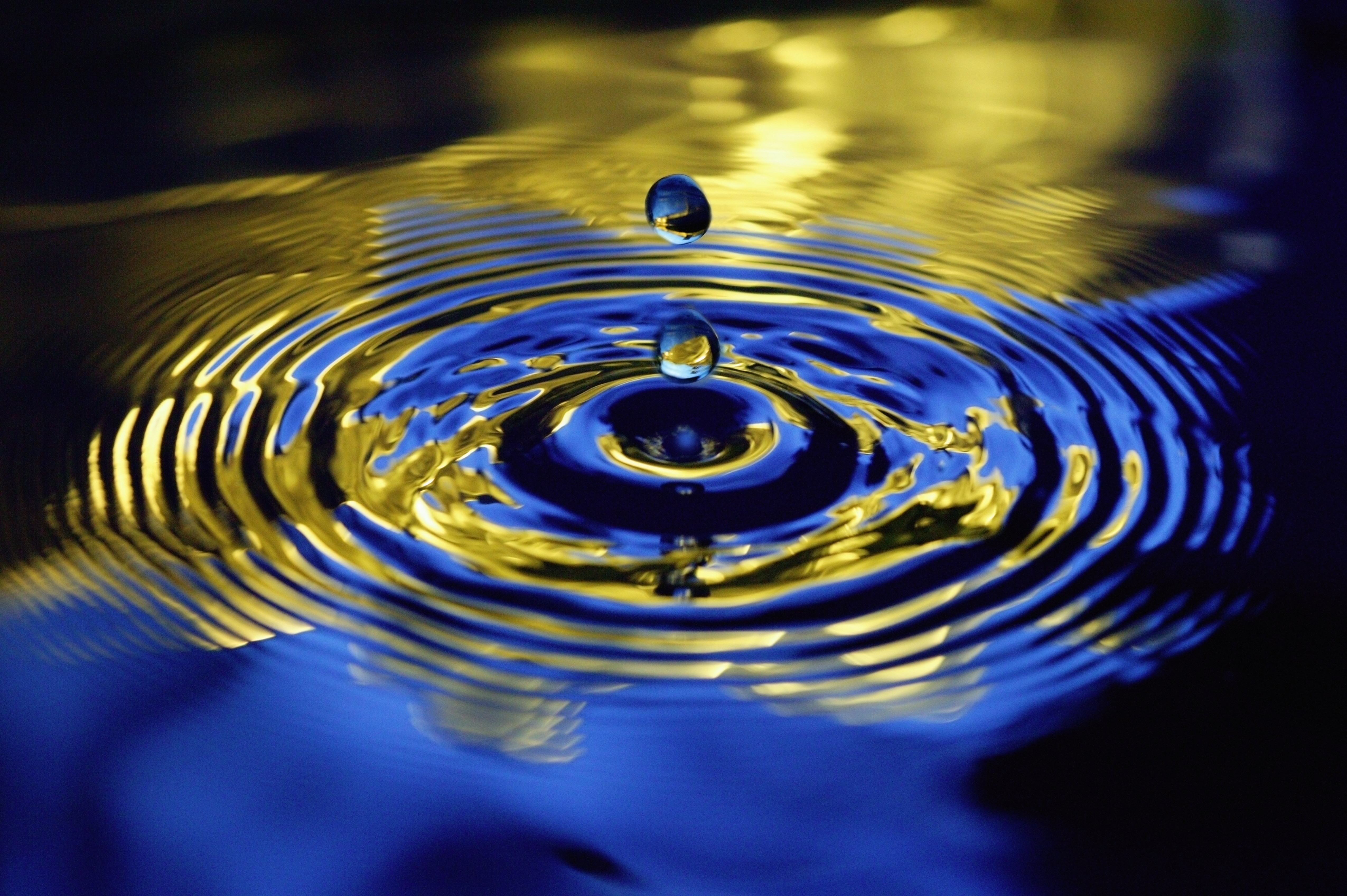 Water droplets falling towards rippled water, close-up