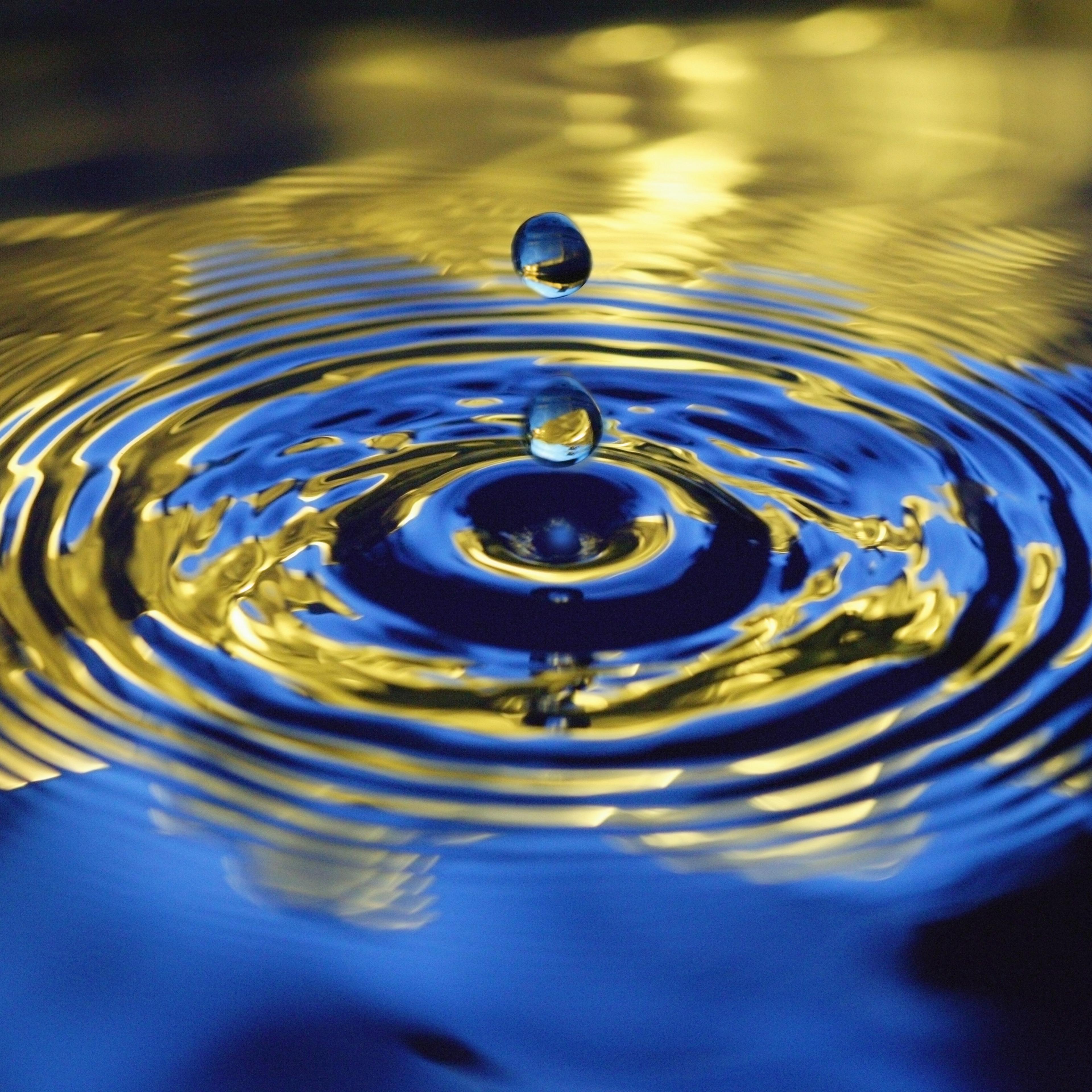 Water droplets falling towards rippled water, close-up