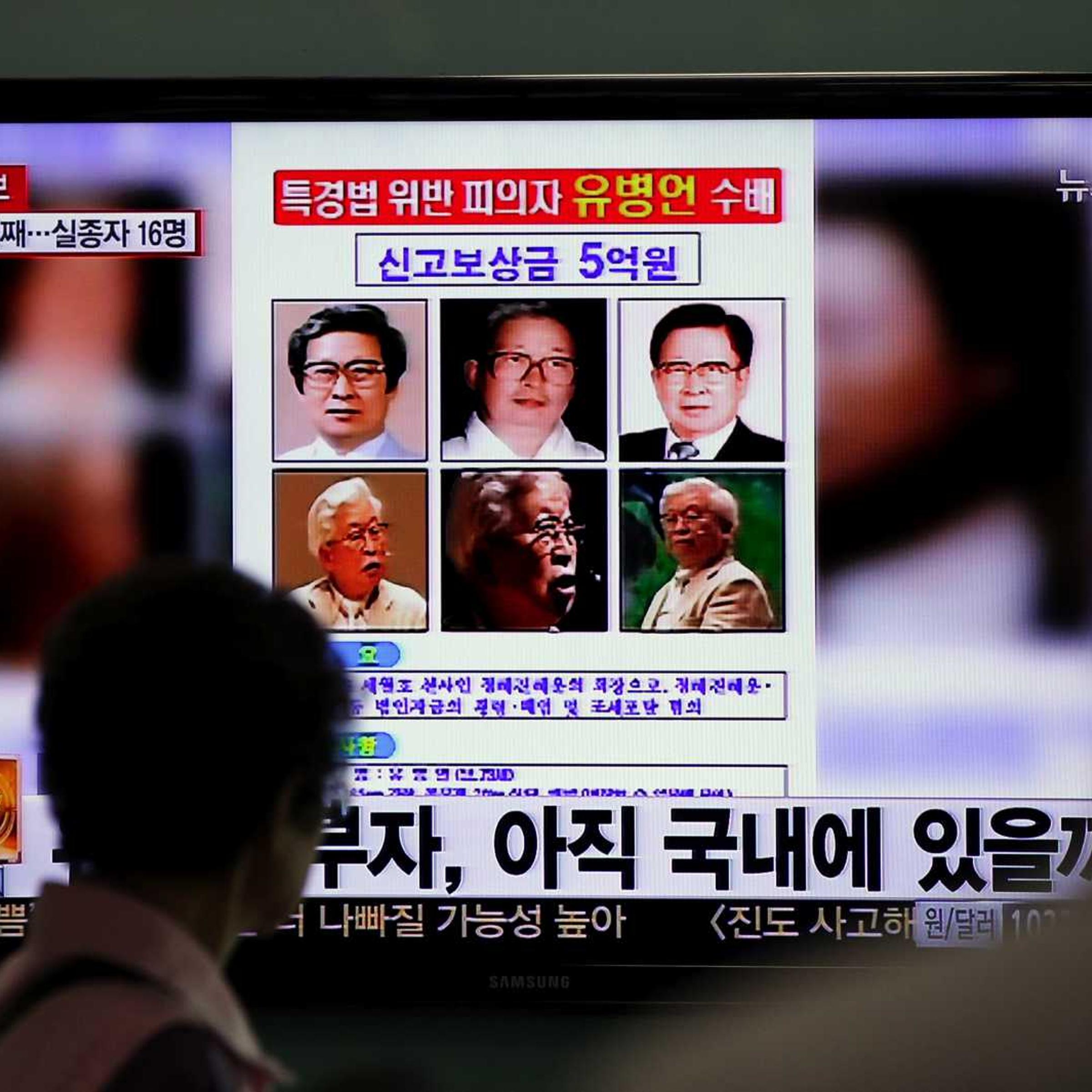 Commuters at a train station in Seoul walk past a screen displaying the wanted poster for Yoo Byung-eun and others, on Monday, May 26, 2014.