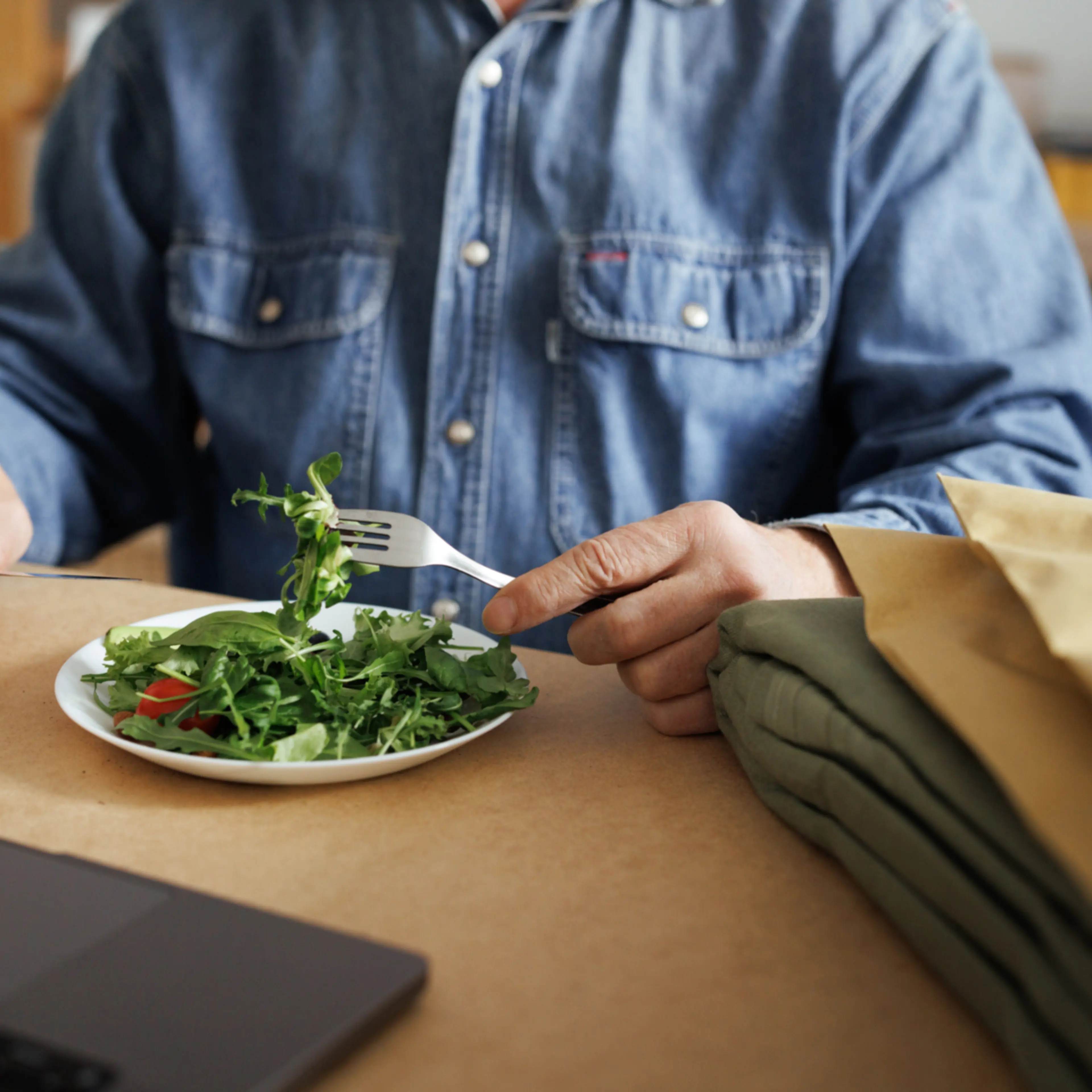 Unrecognizable senior man eating salad while working at home