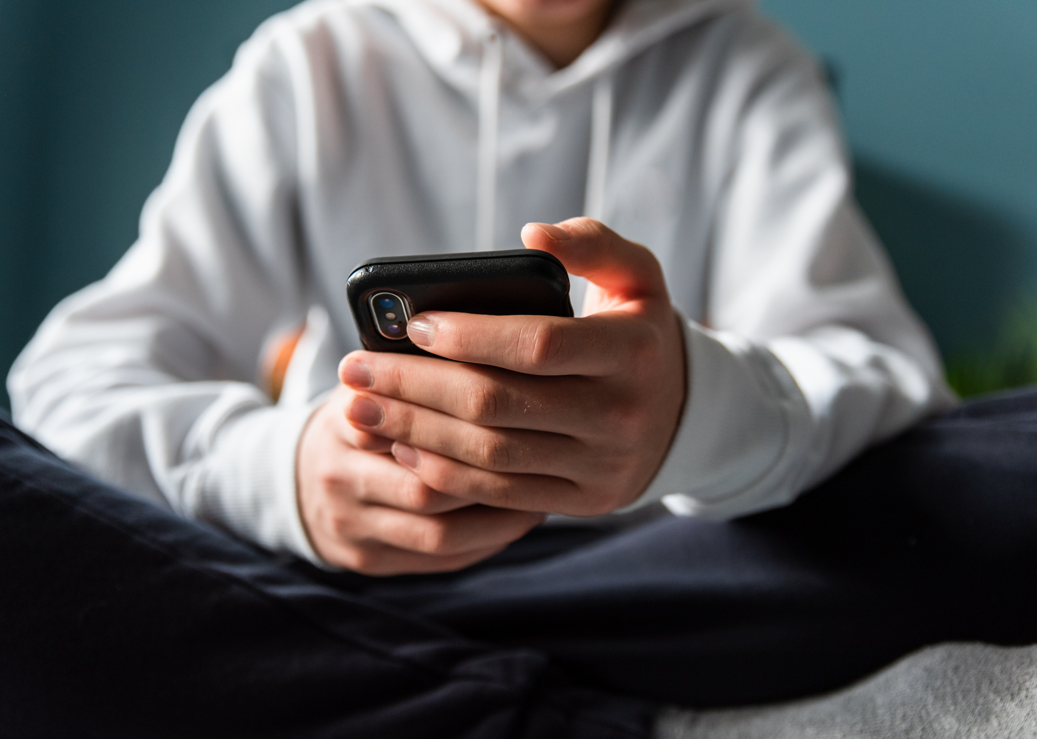 Close up of hands of teen boy in white sweater texting on phone.