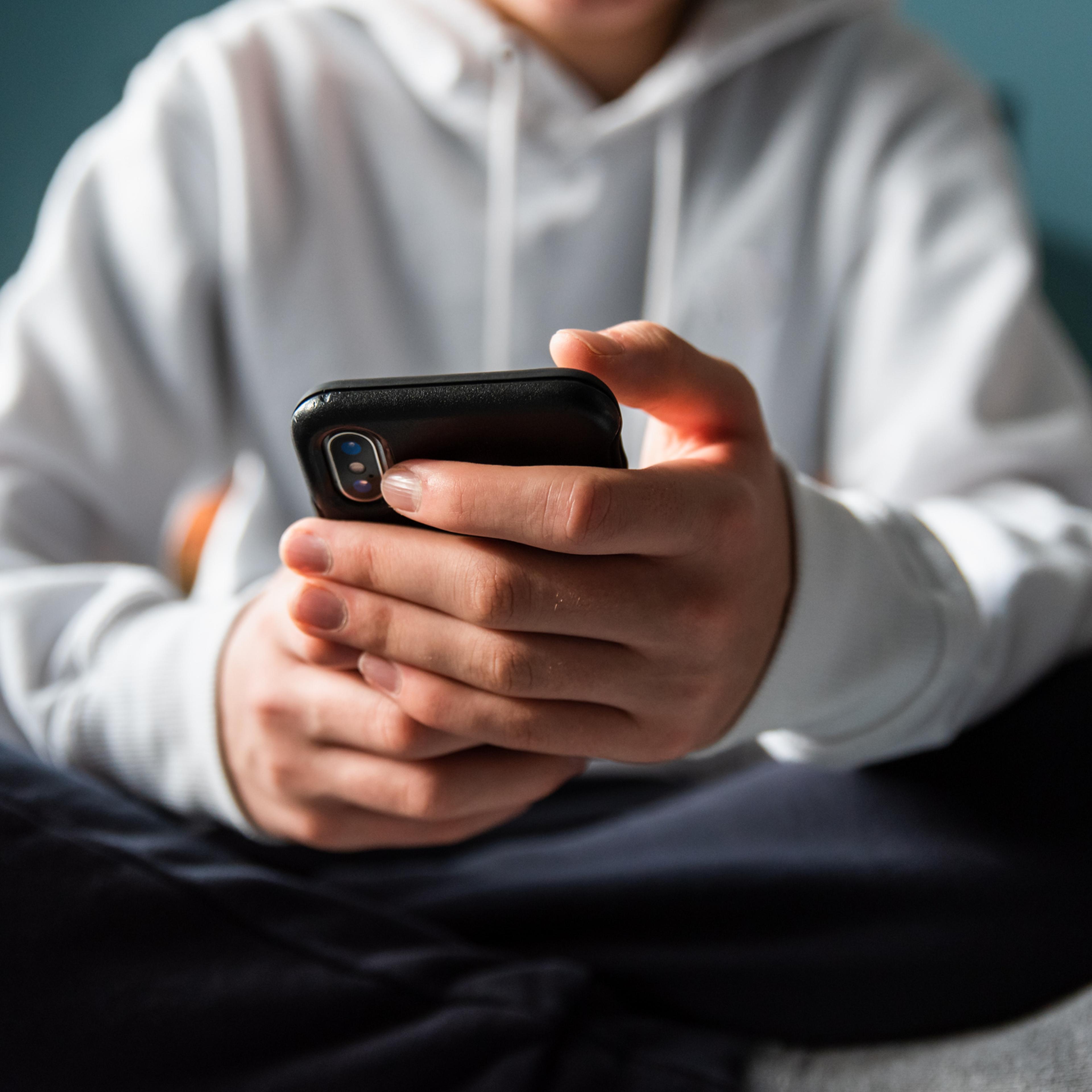 Close up of hands of teen boy in white sweater texting on phone.