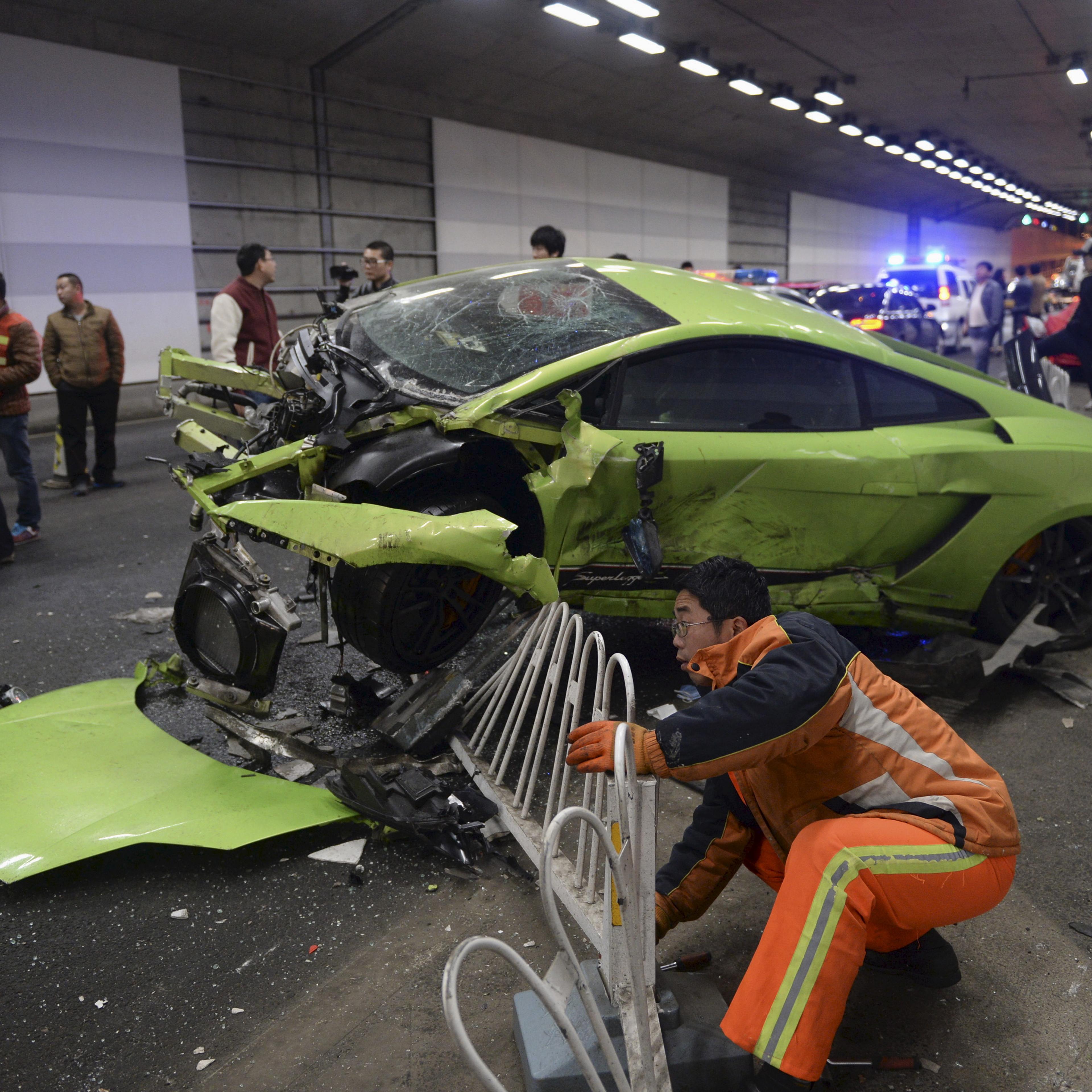 A rescuer tries to remove a part of a broken fence below a damaged Lamborghini after it collided with a Ferrari inside a tunnel in Beijing