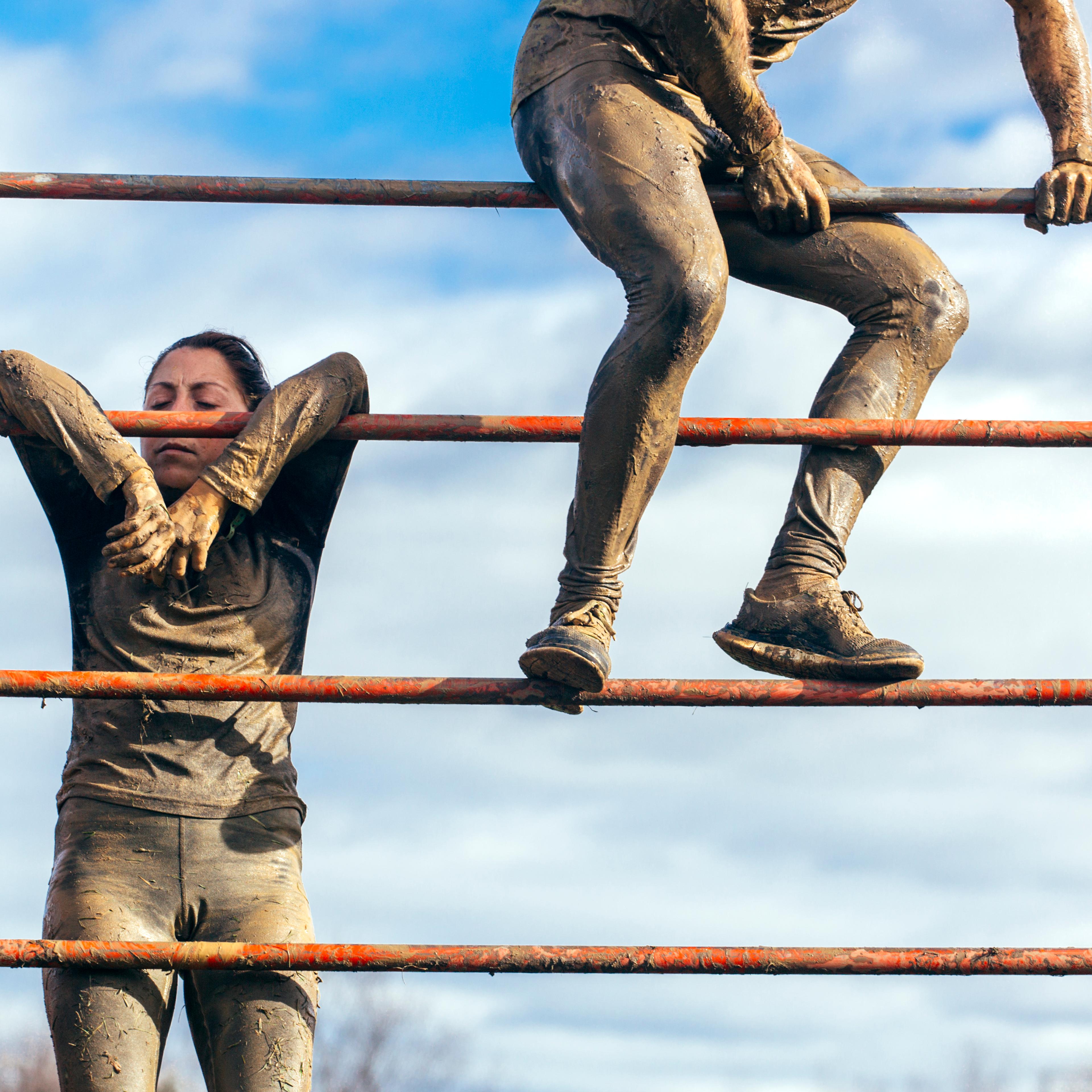Participants in extreme obstacle race climbing over hurdle