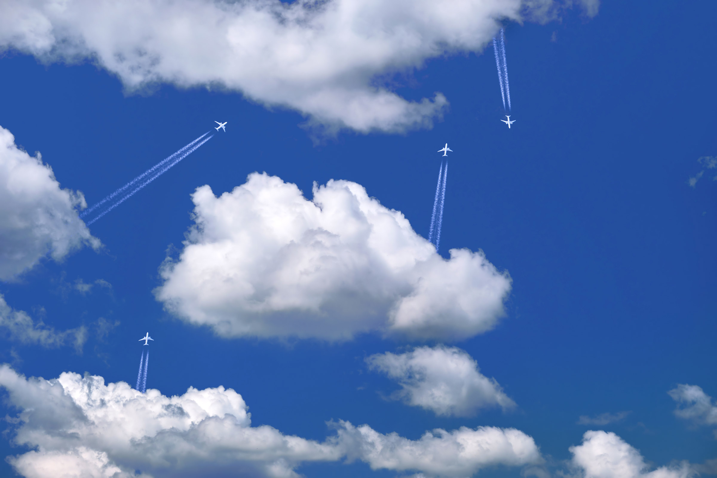 Many distant passenger jet planes flying on high altitude on clear blue sky leaving white smoke trace of contrail behind. Busy air transportation concept