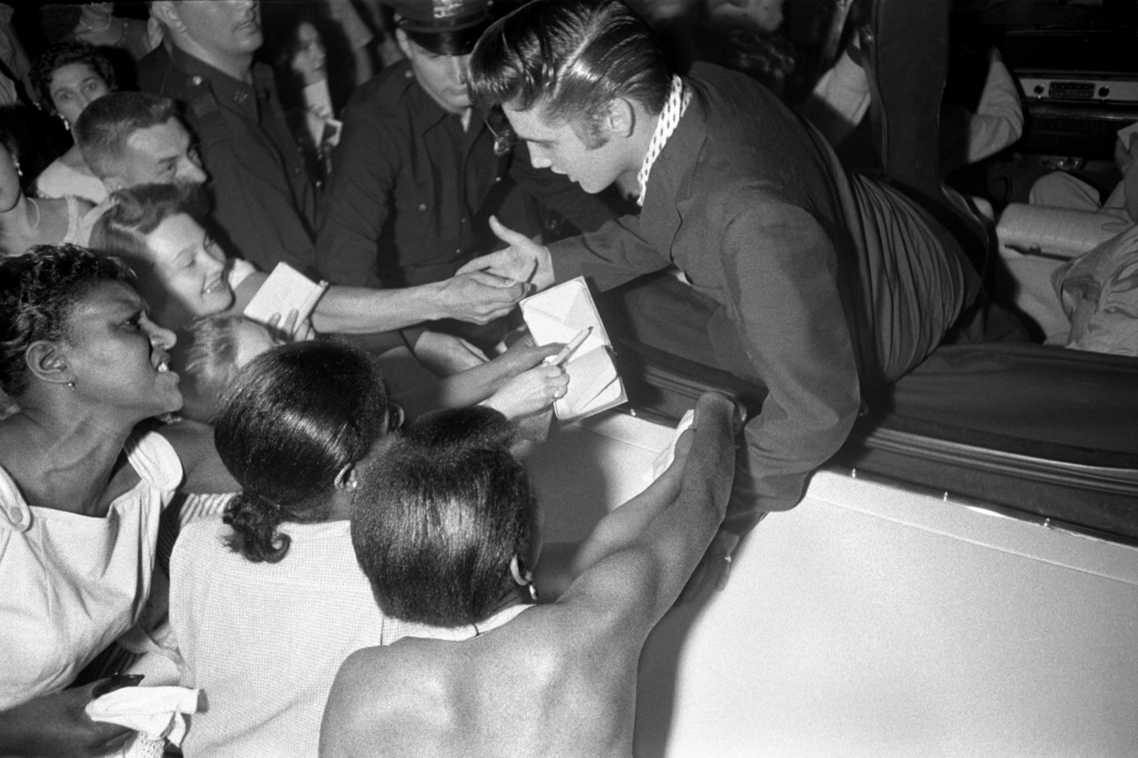 July 1, 1956. The Hudson Theatre, New York. Elvis leaving the theatre where he had performed on the Steve Allen show. This one is unusual...the black girls who are fans are trying to touch him. You think of Little Richard, but you don’t think of Elvis and black fans.