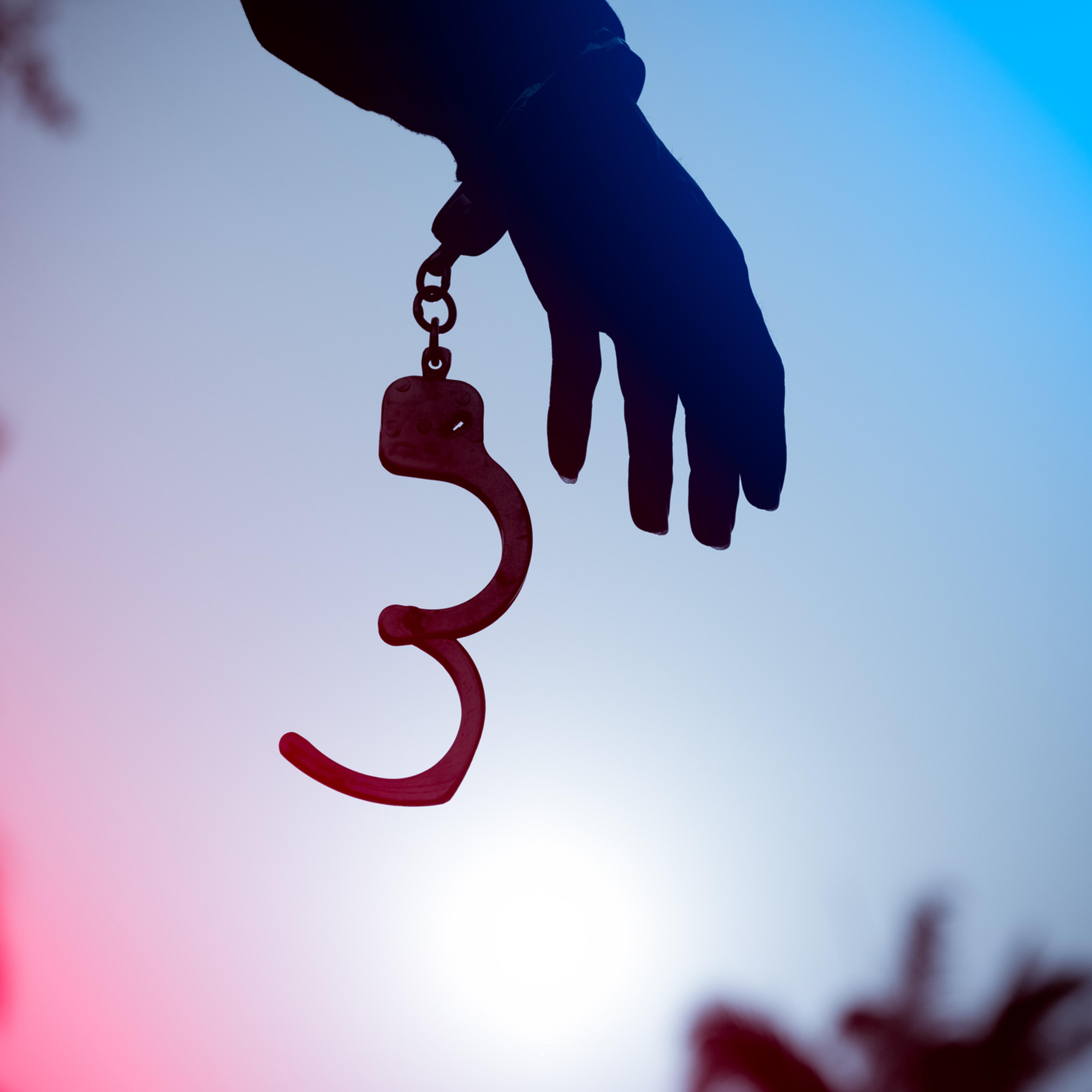 A prisoner behind bars with hands cuffed