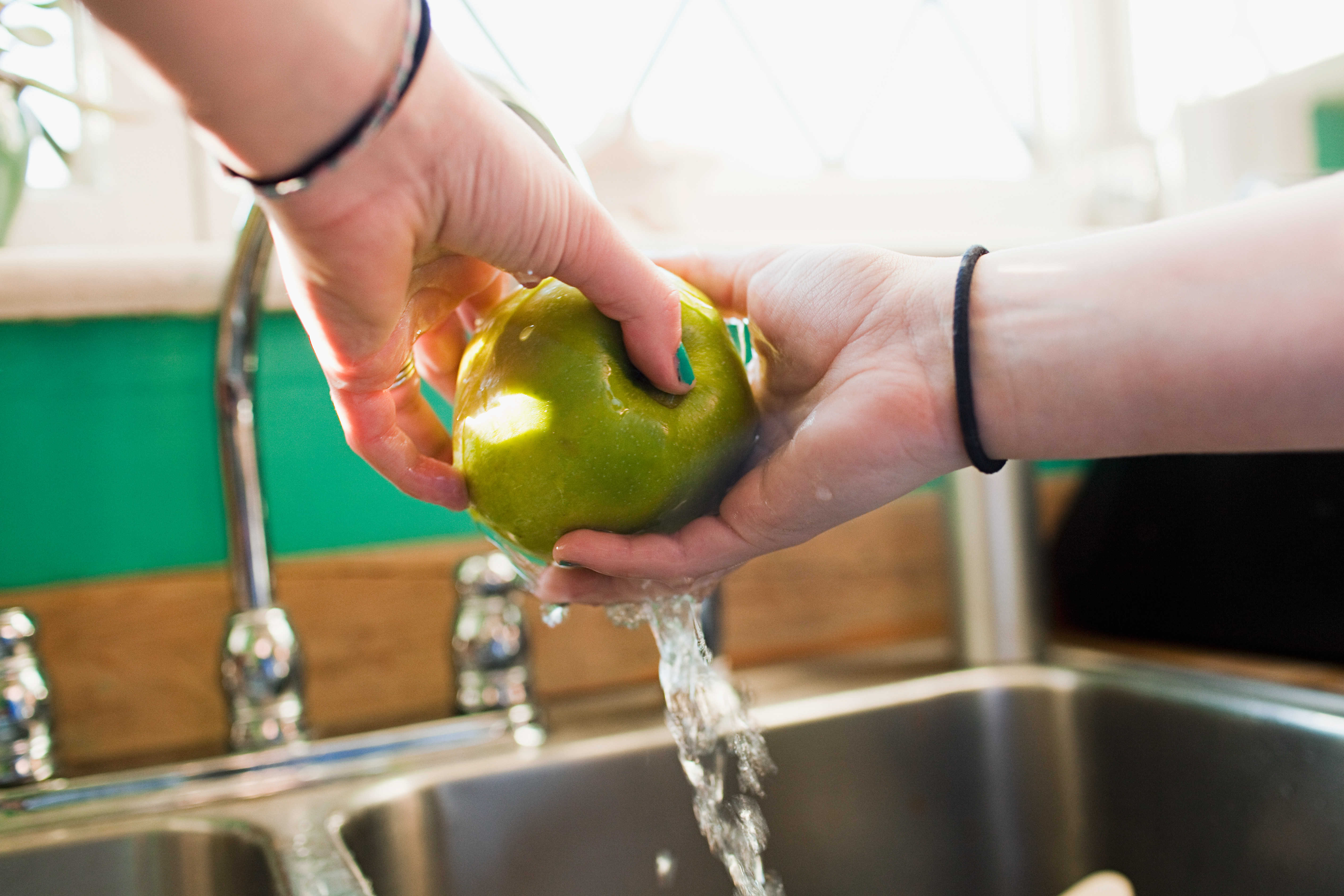 Teenage girl washing apple in kitchen sink