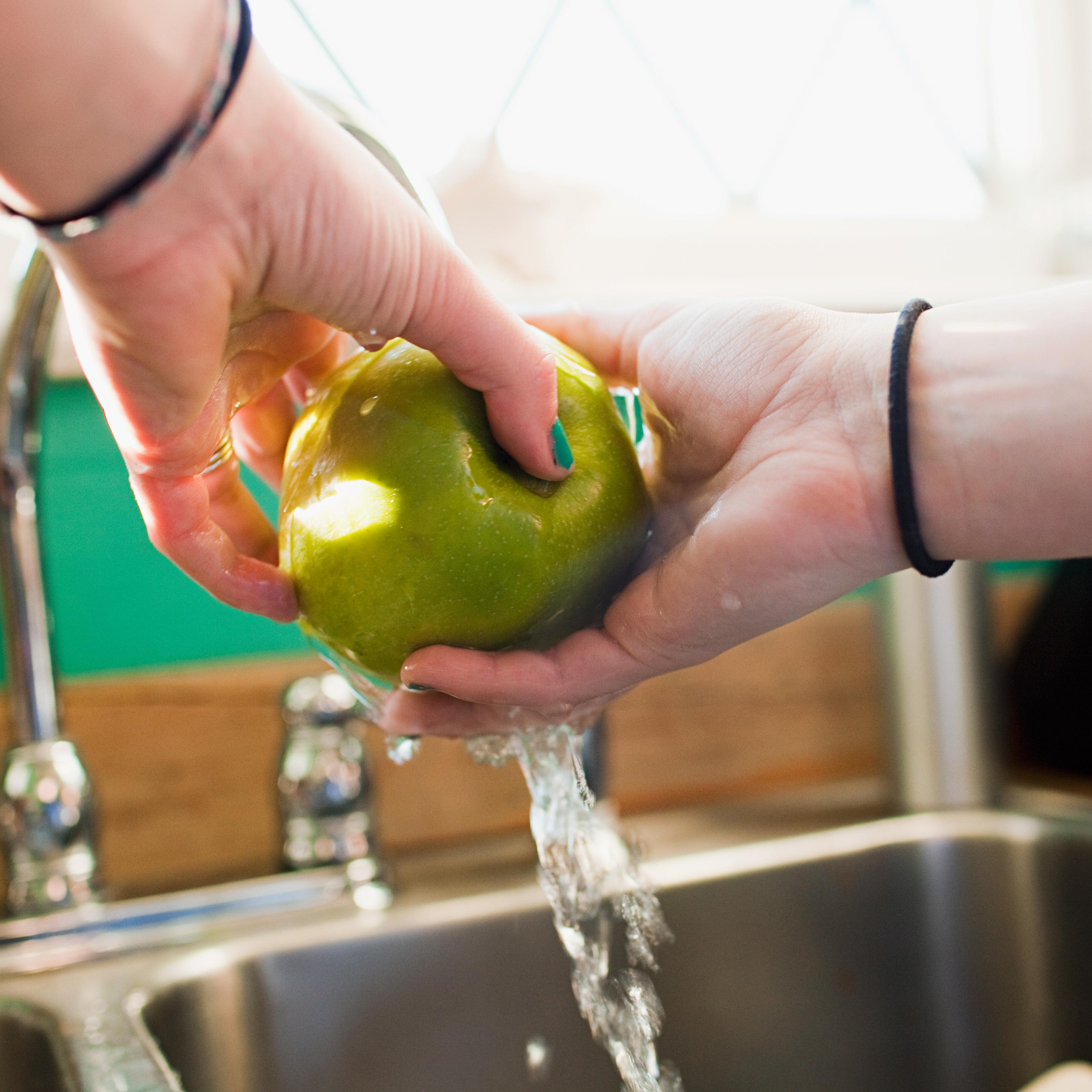 Teenage girl washing apple in kitchen sink