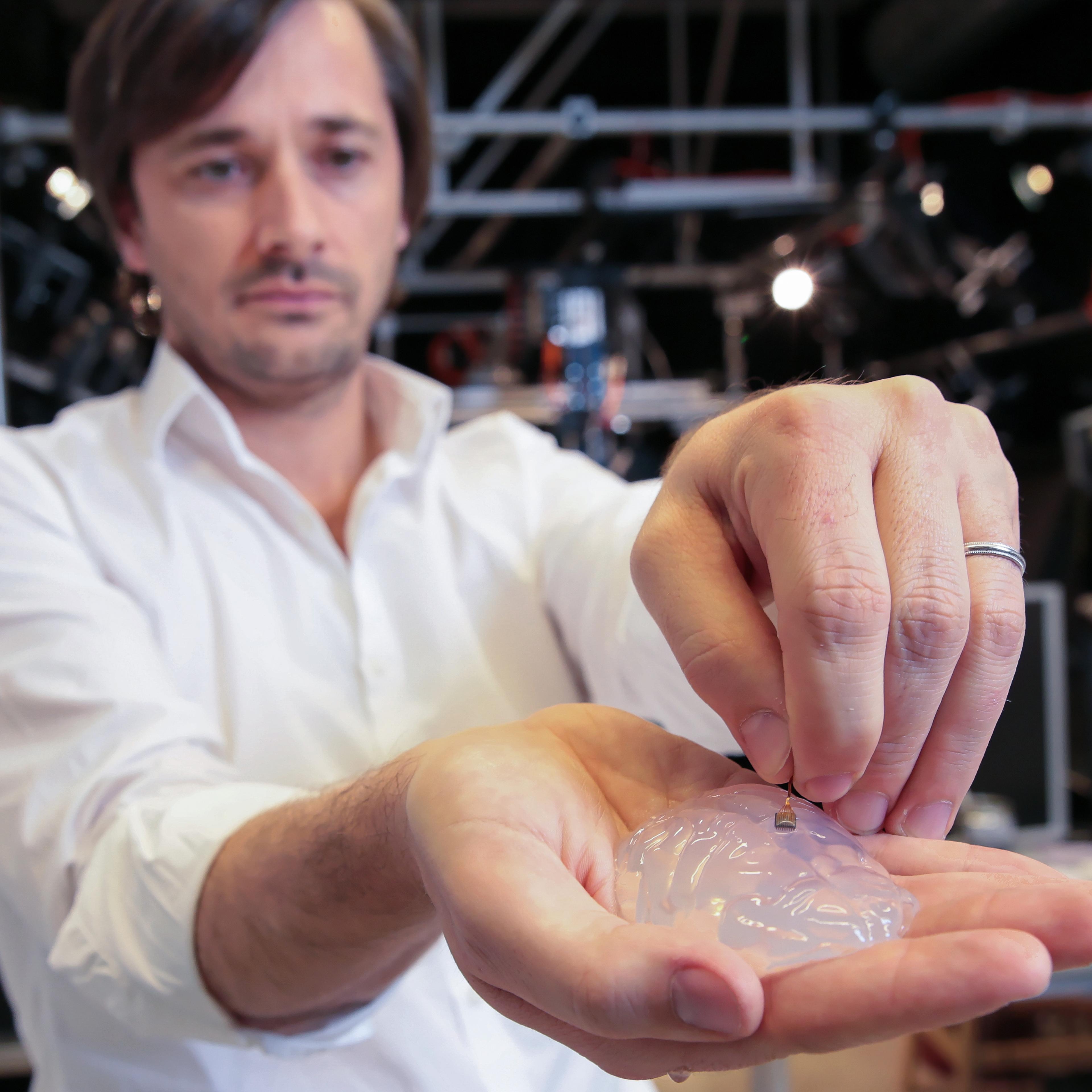 Grégoire Courtine holds a silicon model of a primate’s brain and a brain implant. The brain-spine interface uses a microelectrode array like this one to detect spiking activity of the brain’s motor cortex