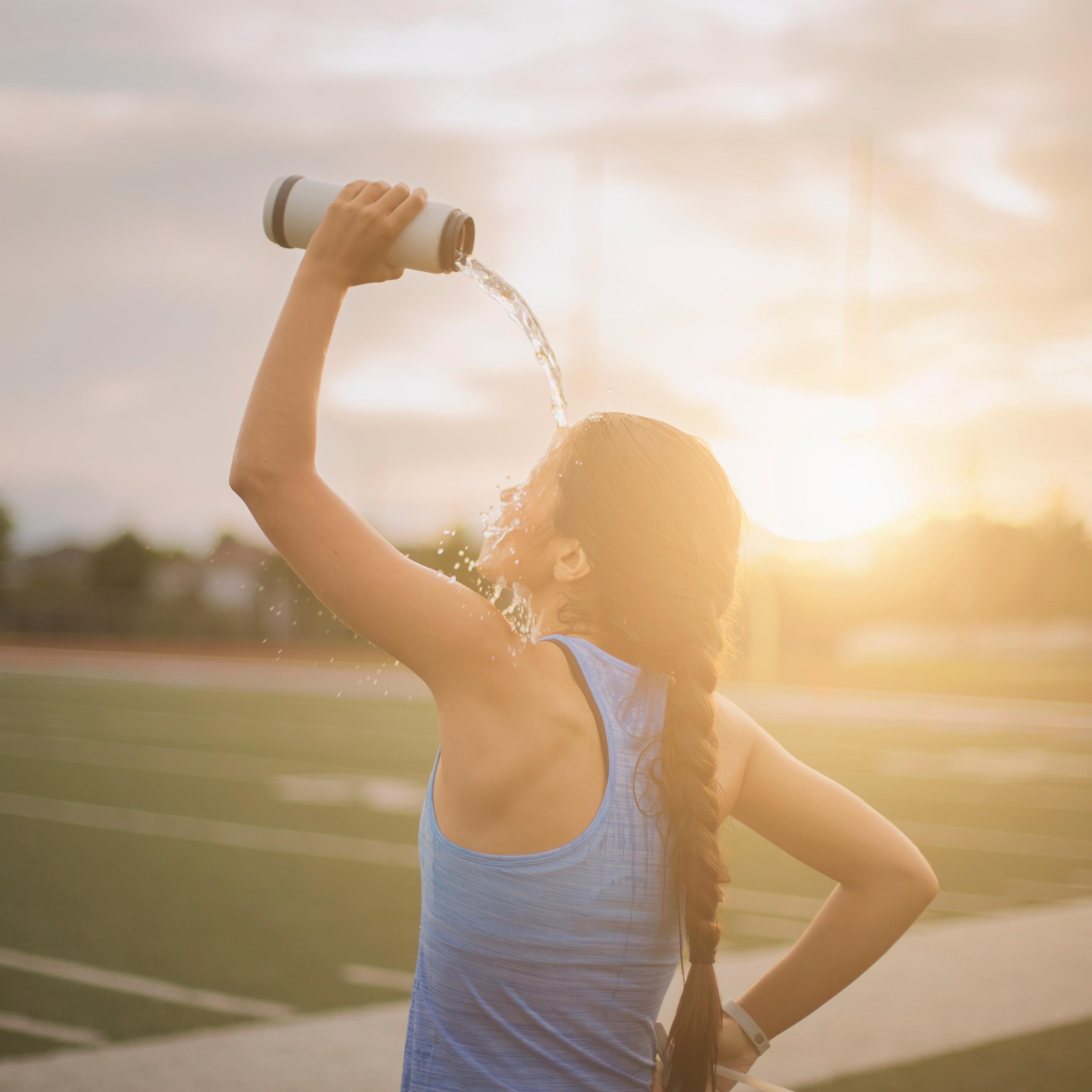 Mixed race athlete pouring water bottle on herself on sports field