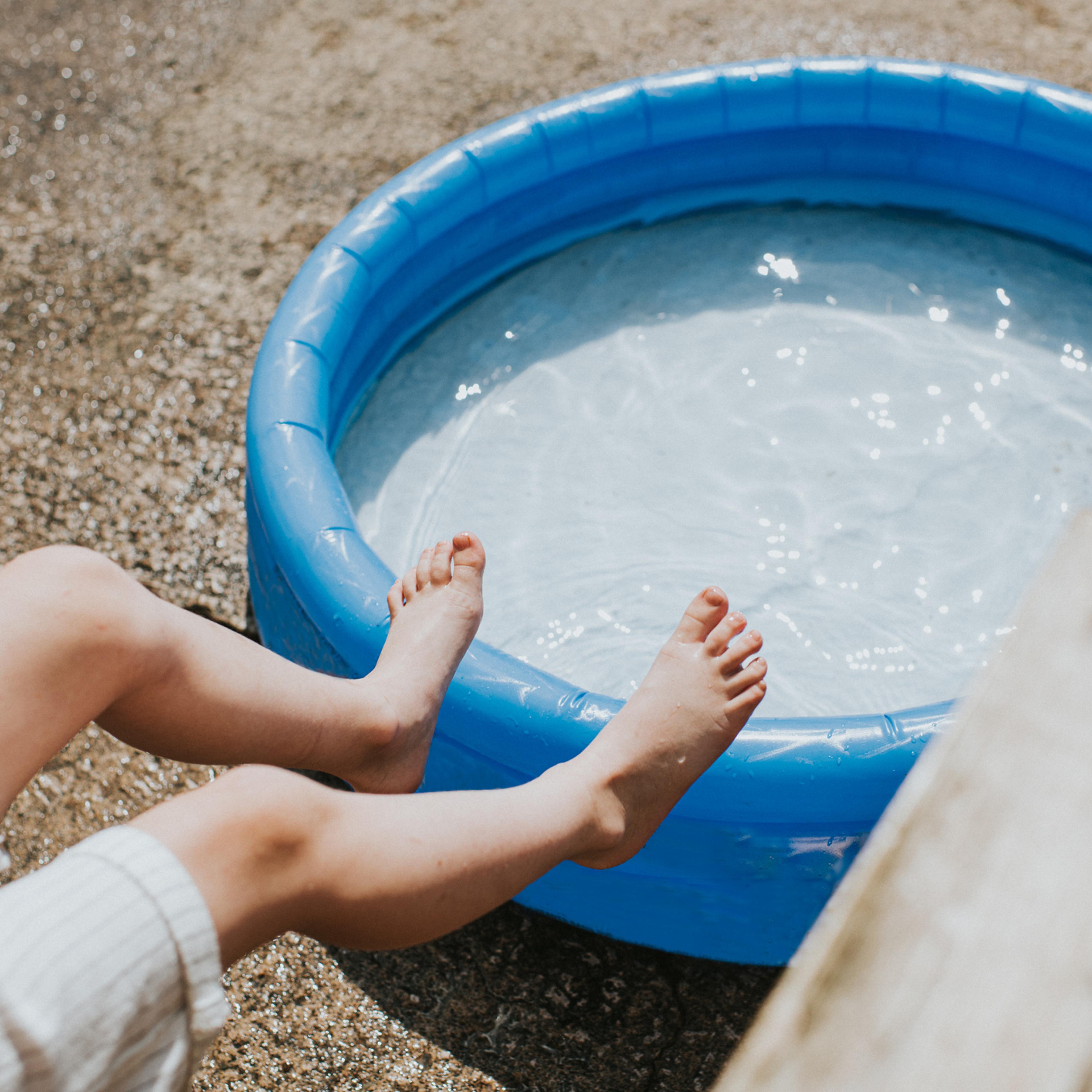 Conceptual image of a child's small feet in mid air over an inflatable paddling pool on a hot day