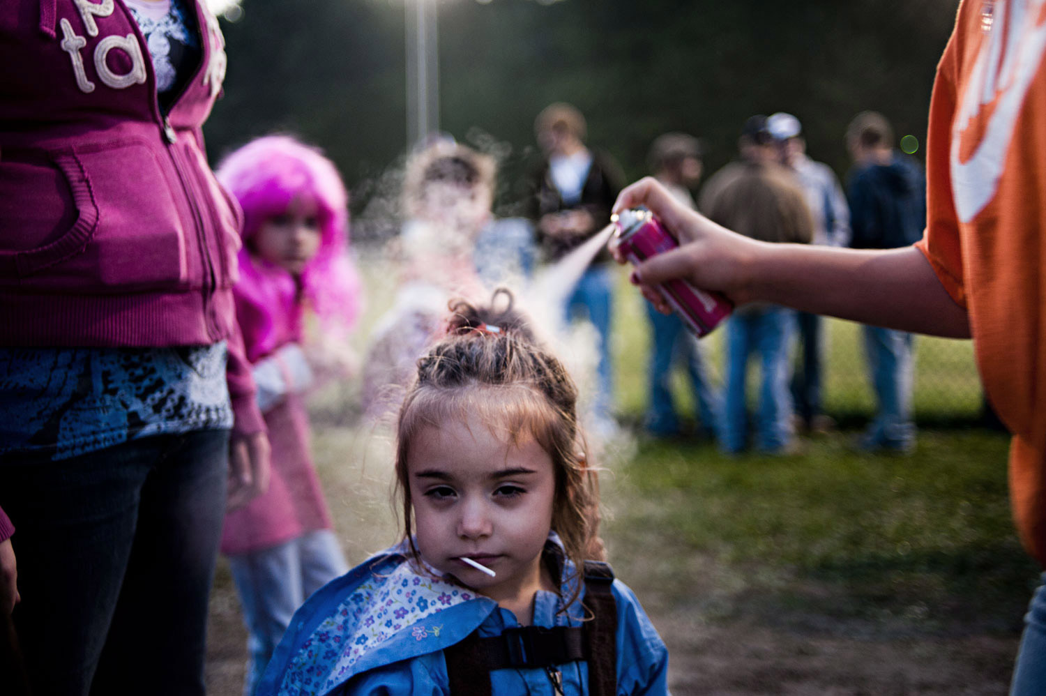 Roxy stands still while her cousins spray her hair pink at a homecoming football game in Glouster, Ohio. There is a 13 year difference between her and her older sister, so the eagerness to fit in with the older girls is persistent. 