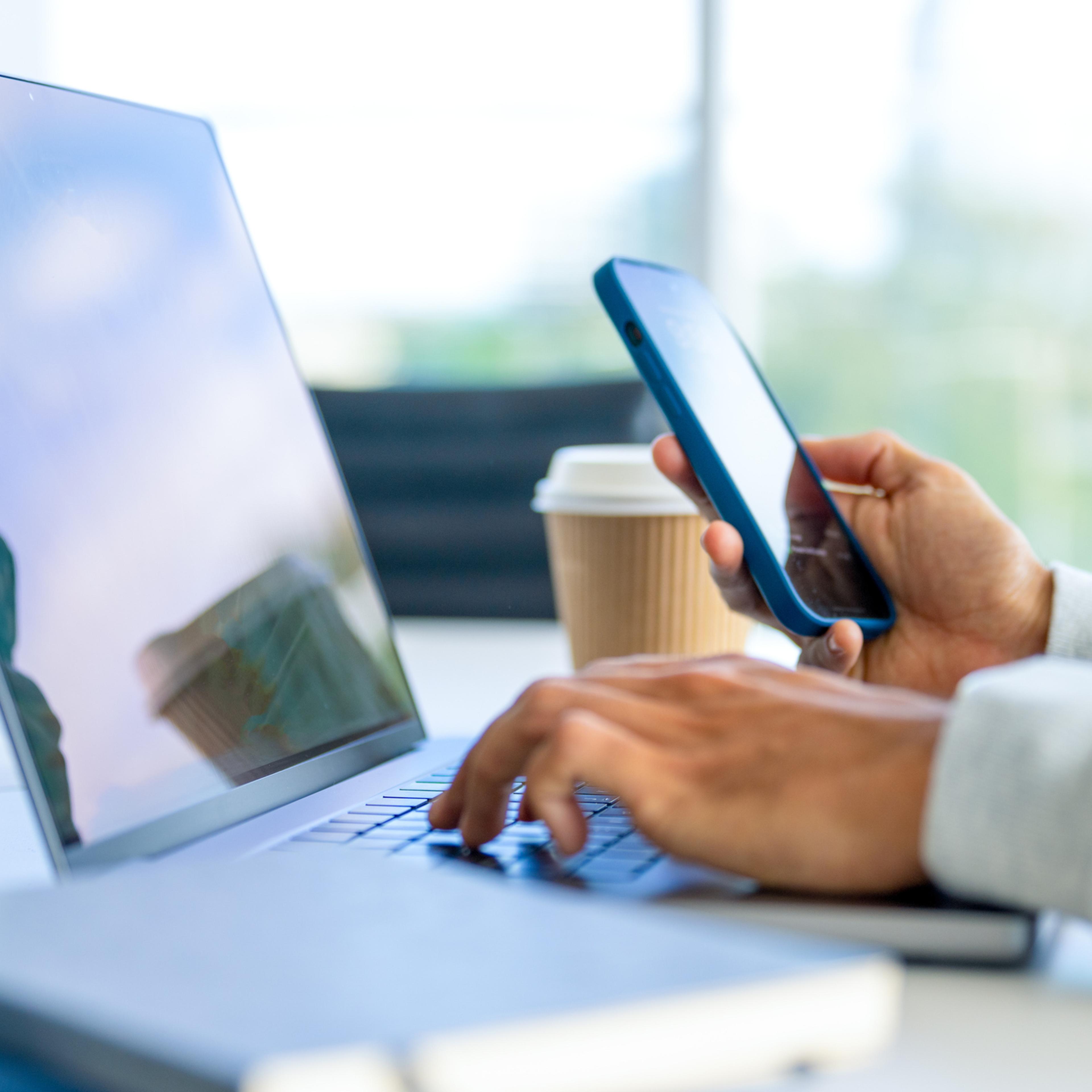 Close up of a Businessman working on a laptop computer and holding and looking at a mobile phone in the office.