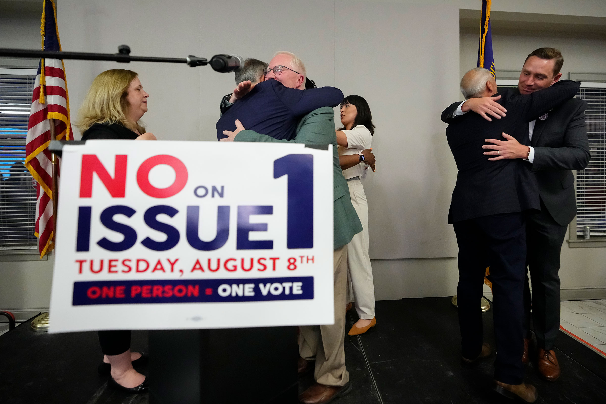 Organizers hug each other with a sign in front of them that says No on Issue 1
