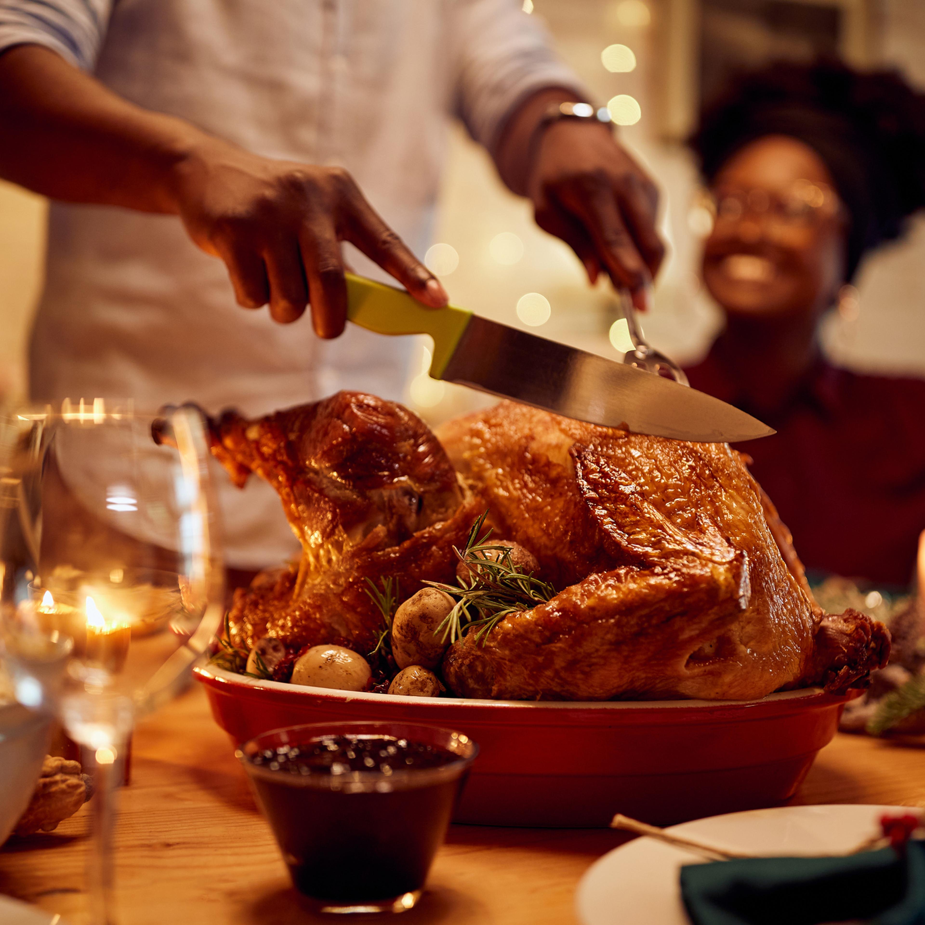 Close-up of African American man carving roasted Thanksgiving turkey.
