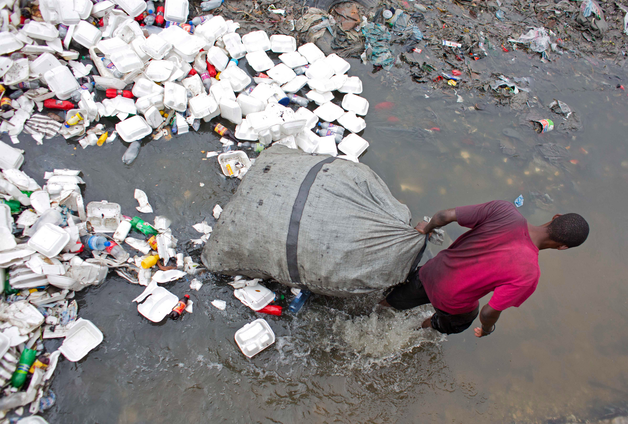 In this Feb. 28, 2016 photo, man wades through a garbage filled water canal pulling his bag after collecting empty bottles to sell, in downtown of Port-au-Prince, Haiti. Scientists believe cholera was introduced to the country's biggest river by inadequa