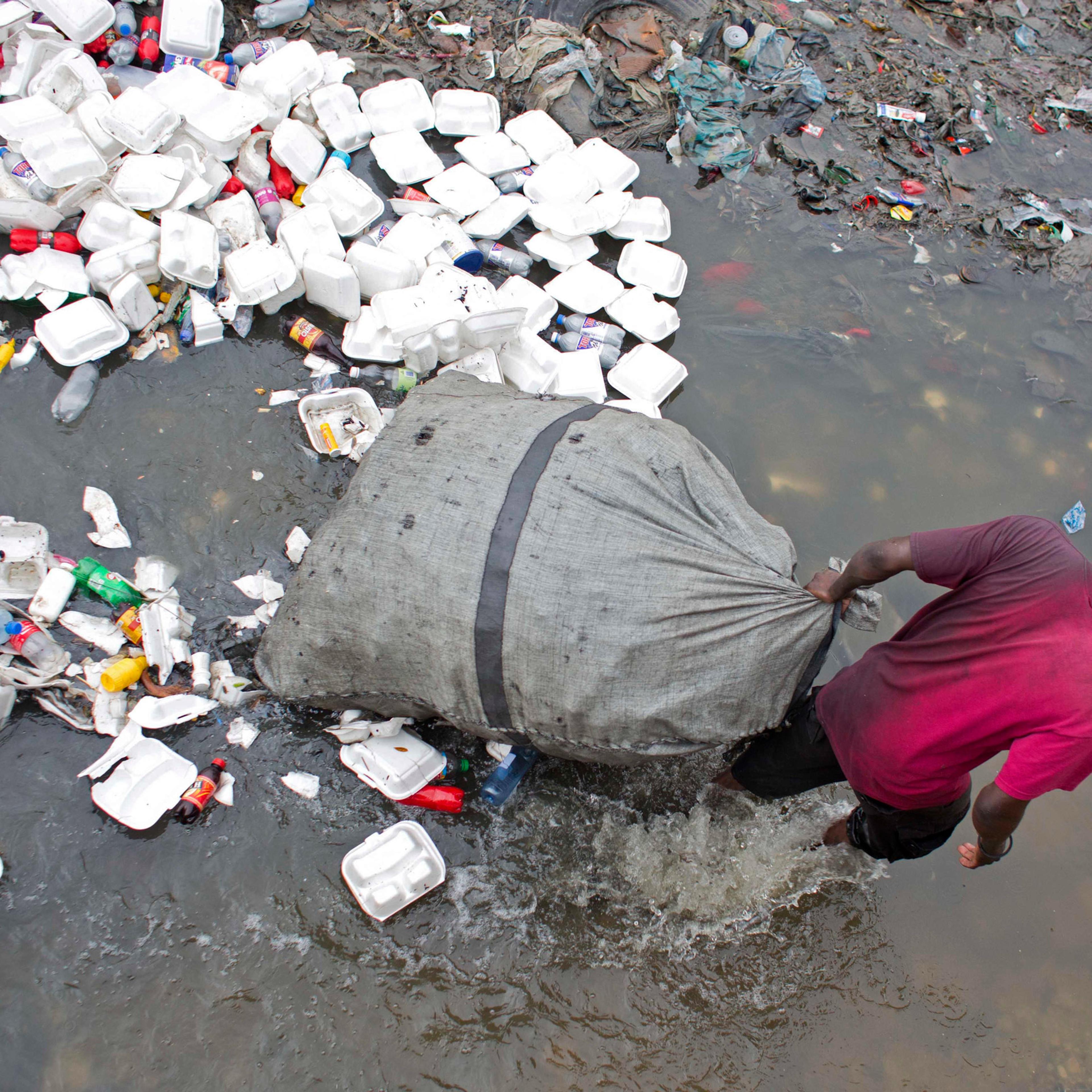 In this Feb. 28, 2016 photo, man wades through a garbage filled water canal pulling his bag after collecting empty bottles to sell, in downtown of Port-au-Prince, Haiti. Scientists believe cholera was introduced to the country's biggest river by inadequa