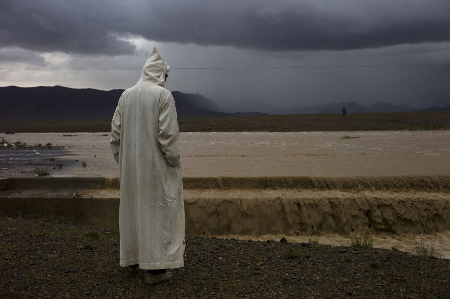 Morocco, 2011. 
A passenger of a bus waits while a flash flood takes out the road ahead of them near the northern edge of the Sahara desert in present-day Morocco