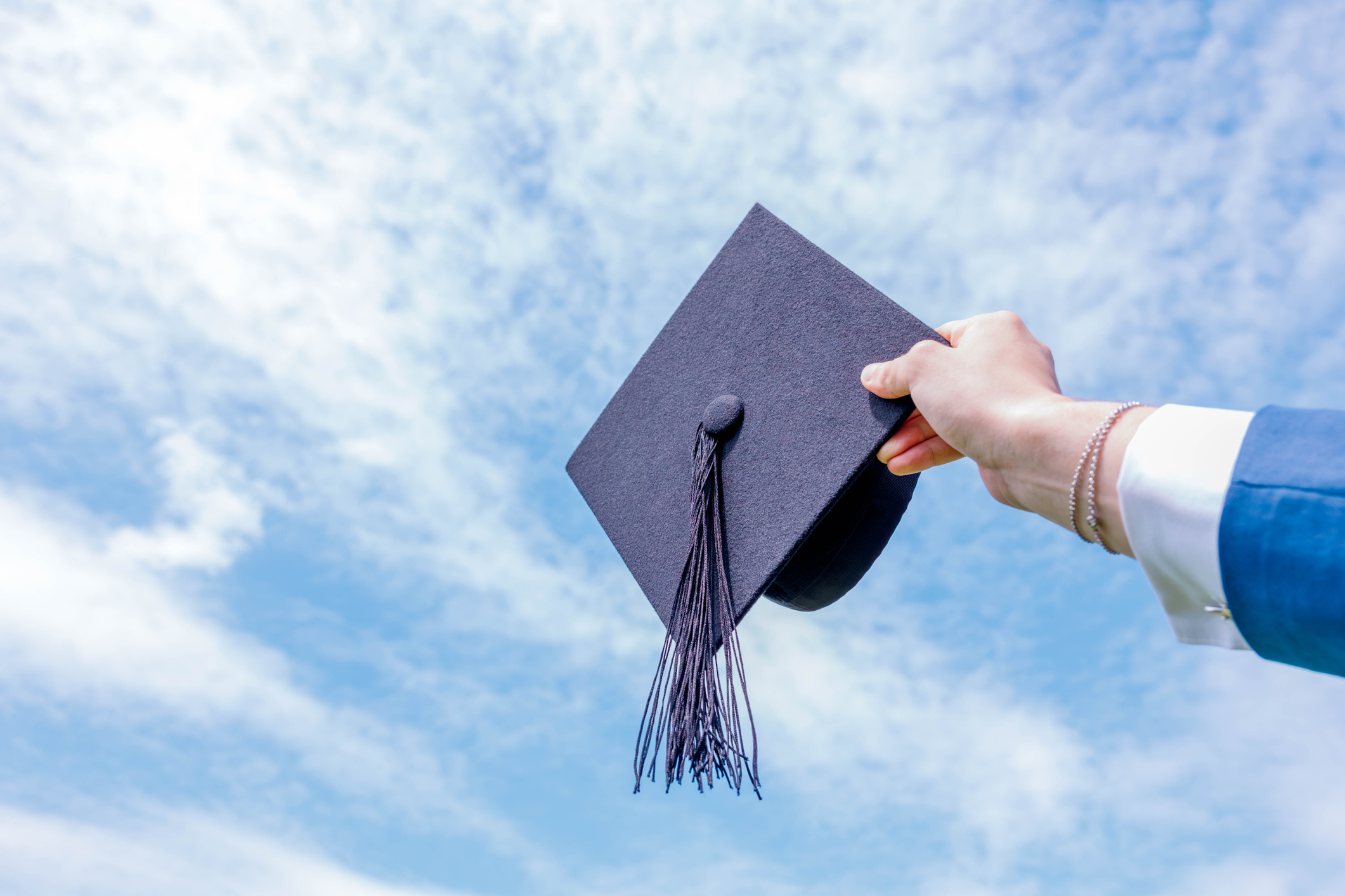 Hand holding graduation hat against a blue sky