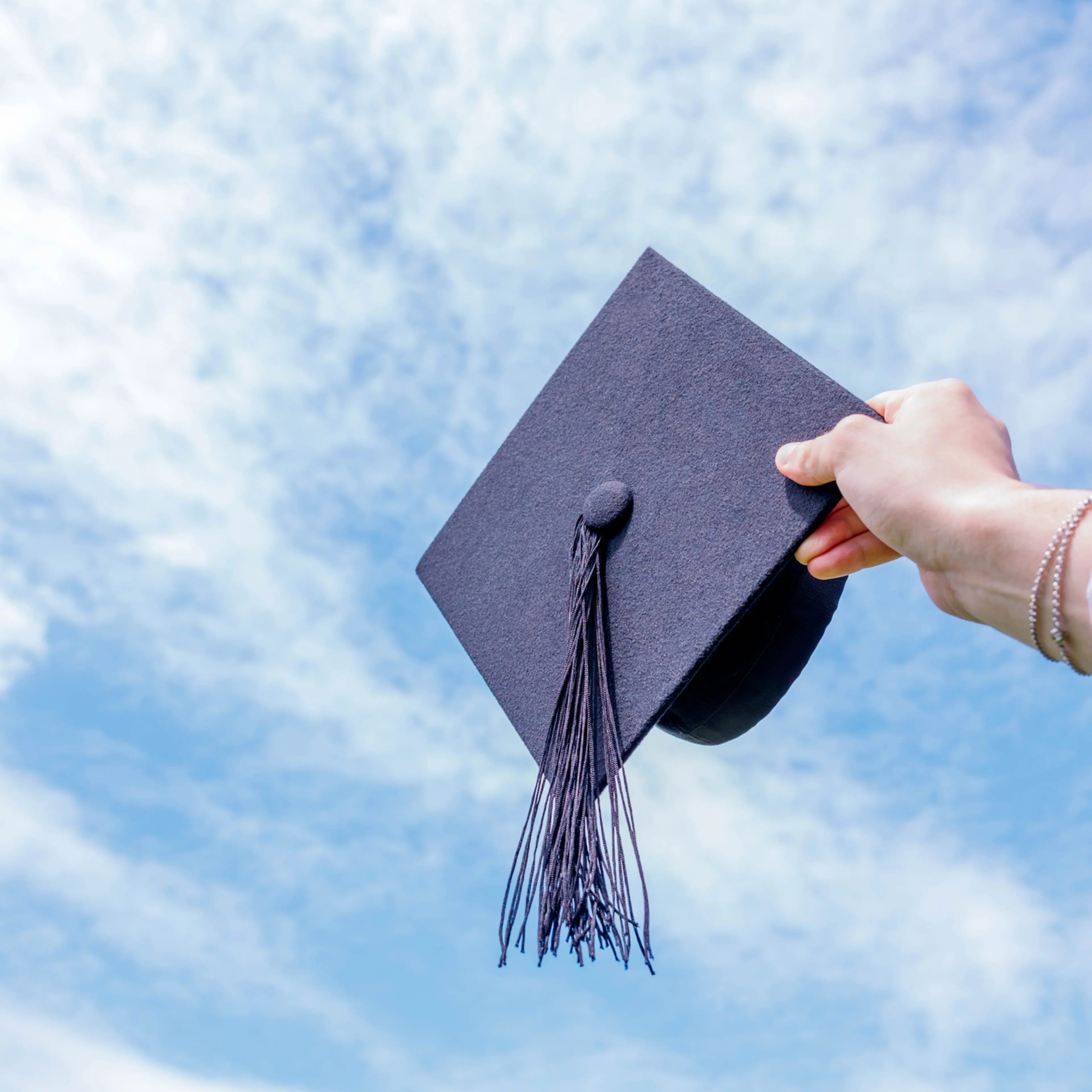 Hand holding graduation hat against a blue sky