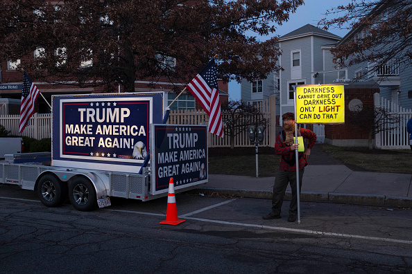A protester stands beside a pro-Trump billboard outside the Sheraton Portsmouth Harborside Hotel where Republican Presidential candidate Donald Trump is due to speak at the New England Police Benevolent Association Meeting December 10, 2015 in Portsmouth
