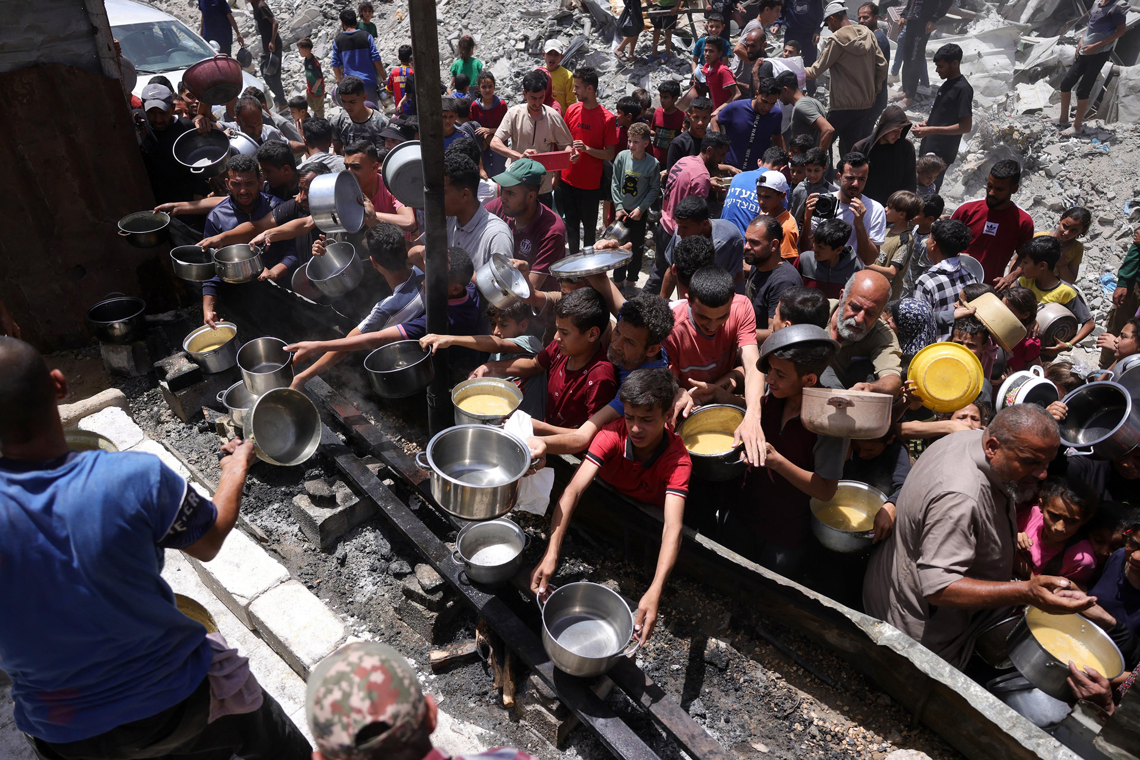 Displaced Palestinians gather to collect portions of cooked food at a charity distribution point in Jabalia in the northern Gaza Strip on May 19, 2025.