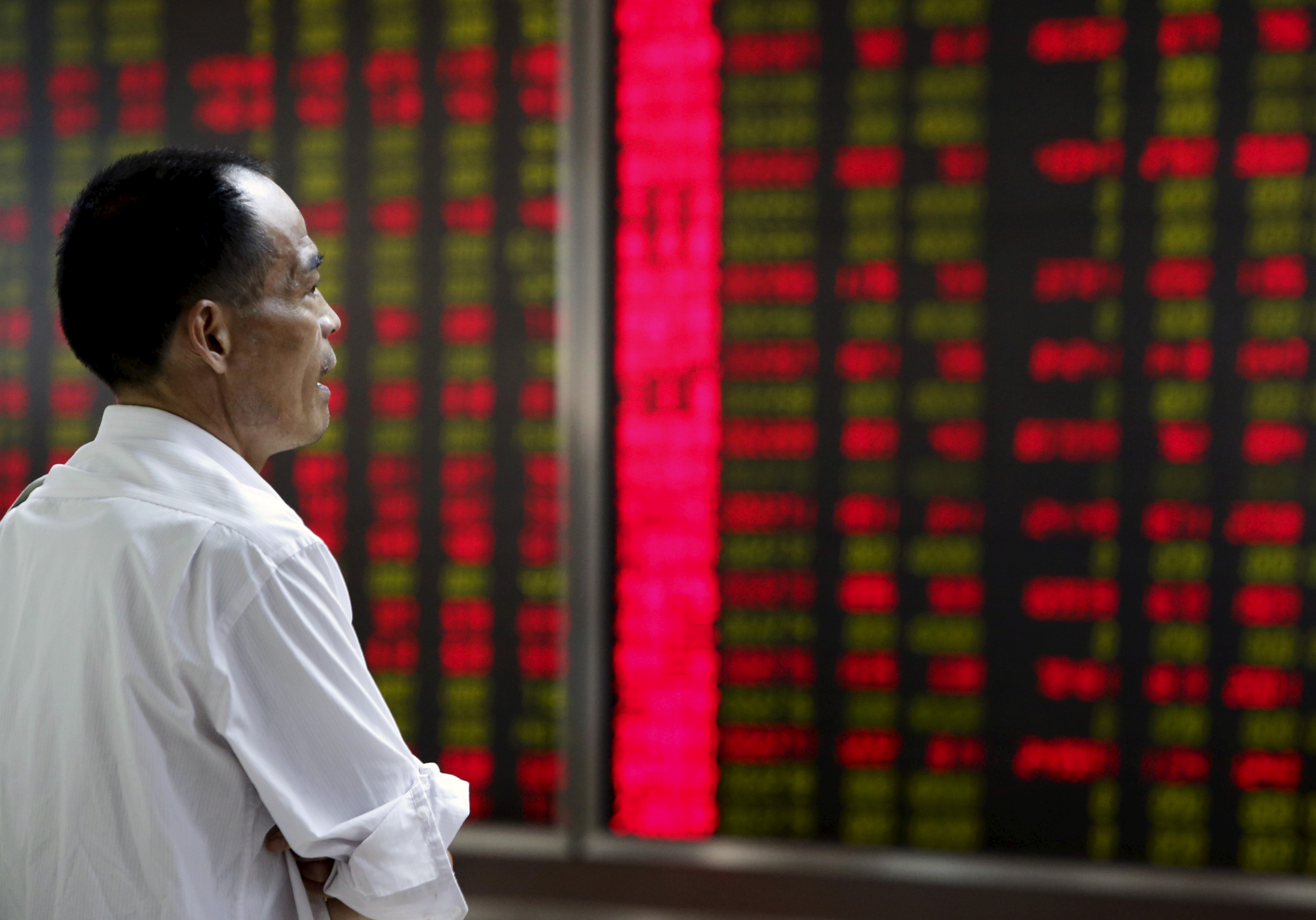 An investor watches an electronic board showing stock information at a brokerage office in Beijing