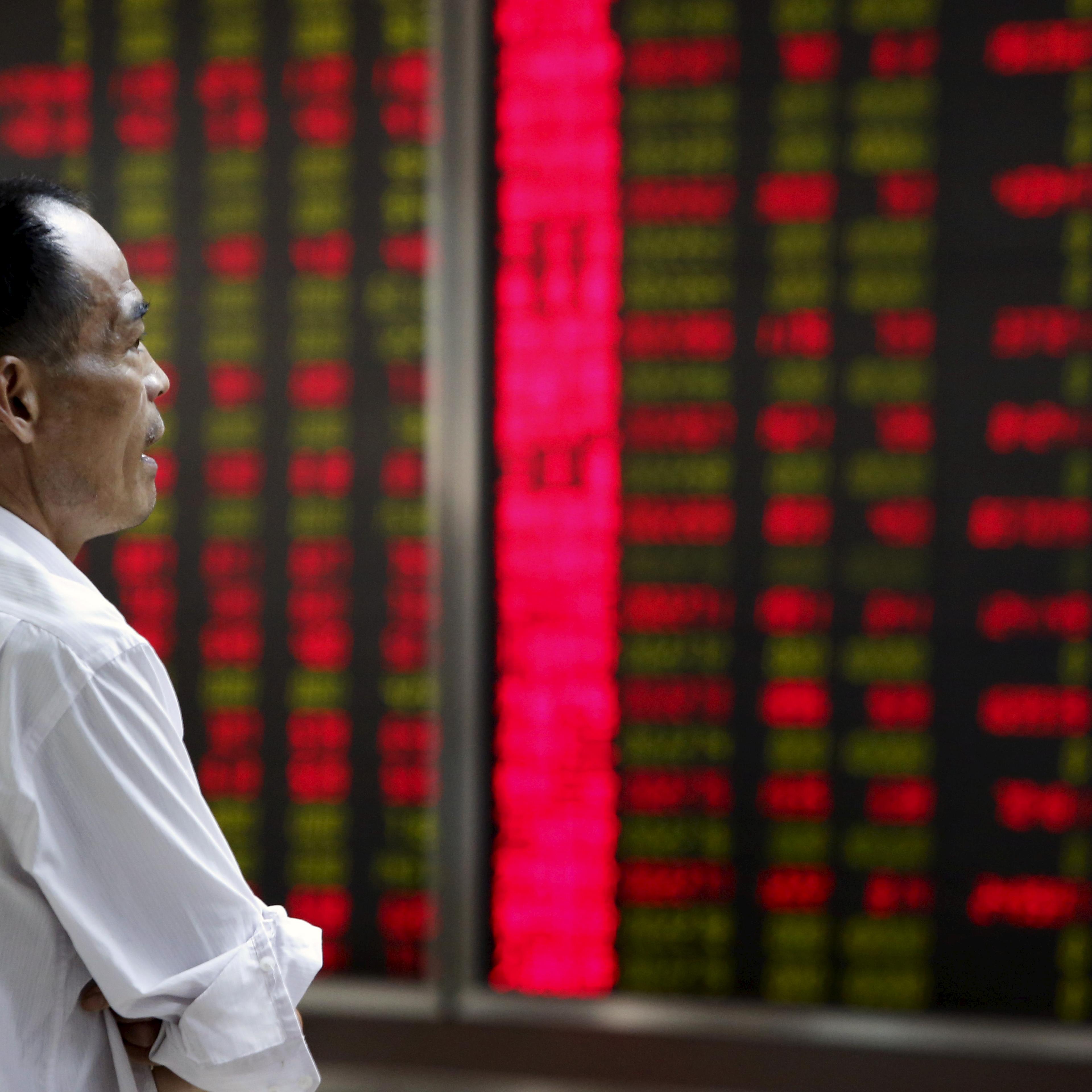 An investor watches an electronic board showing stock information at a brokerage office in Beijing