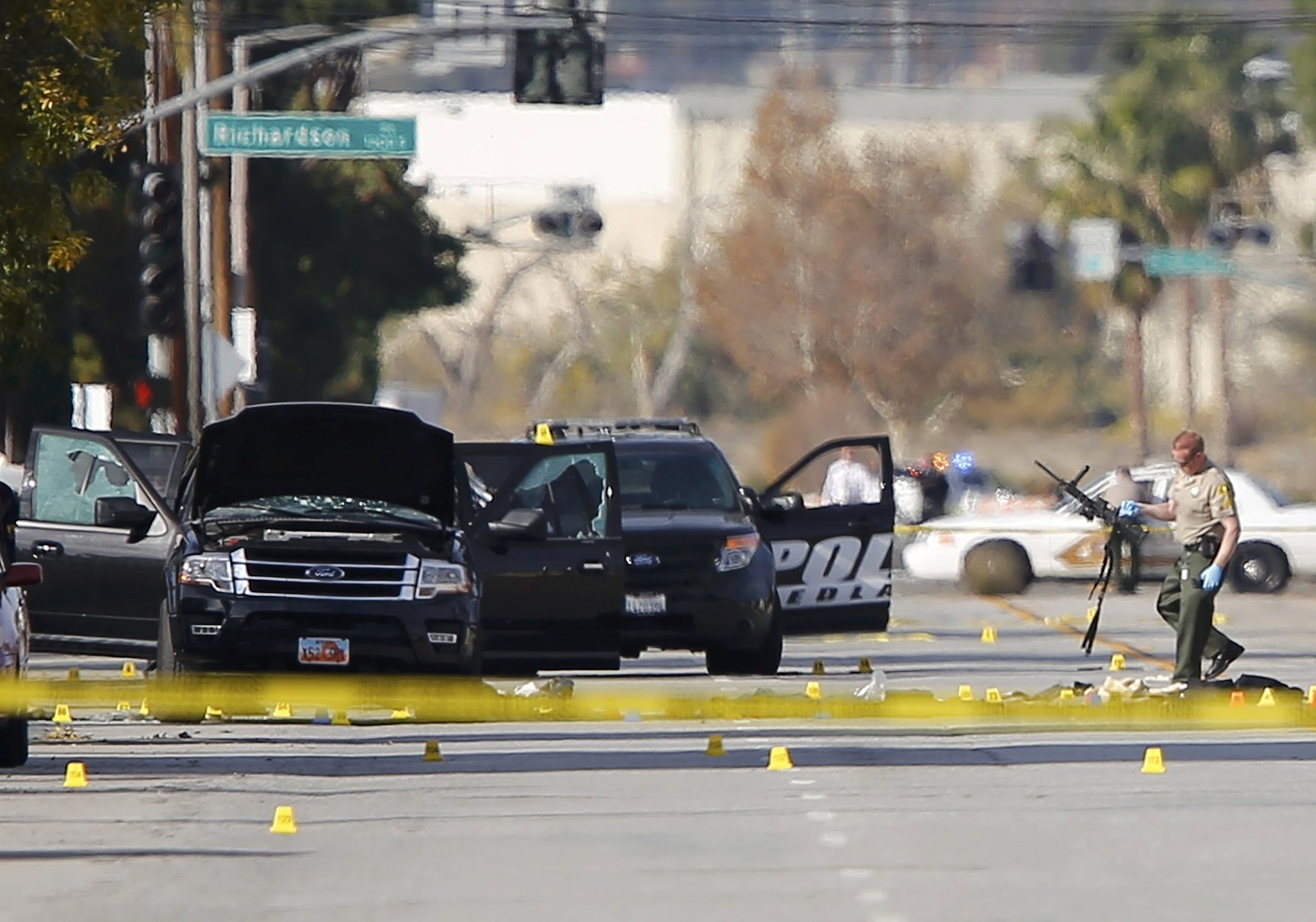A police officer picks up a weapon from the scene of the investigation around the area of the SUV vehicle where two suspects were shot by police following a mass shooting in San Bernardino, Calif. on Dec. 3, 2015.