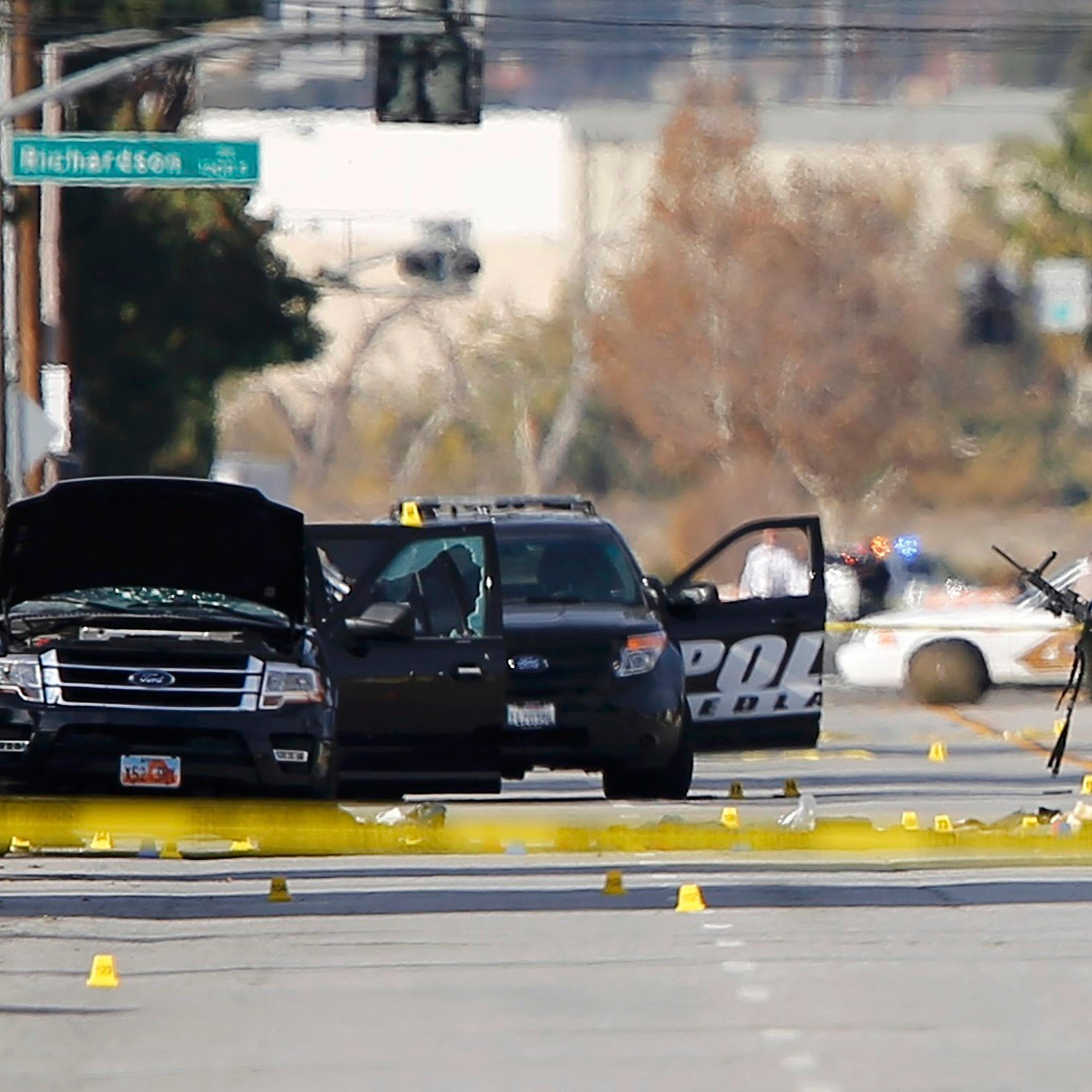 A police officer picks up a weapon from the scene of the investigation around the area of the SUV vehicle where two suspects were shot by police following a mass shooting in San Bernardino, Calif. on Dec. 3, 2015.