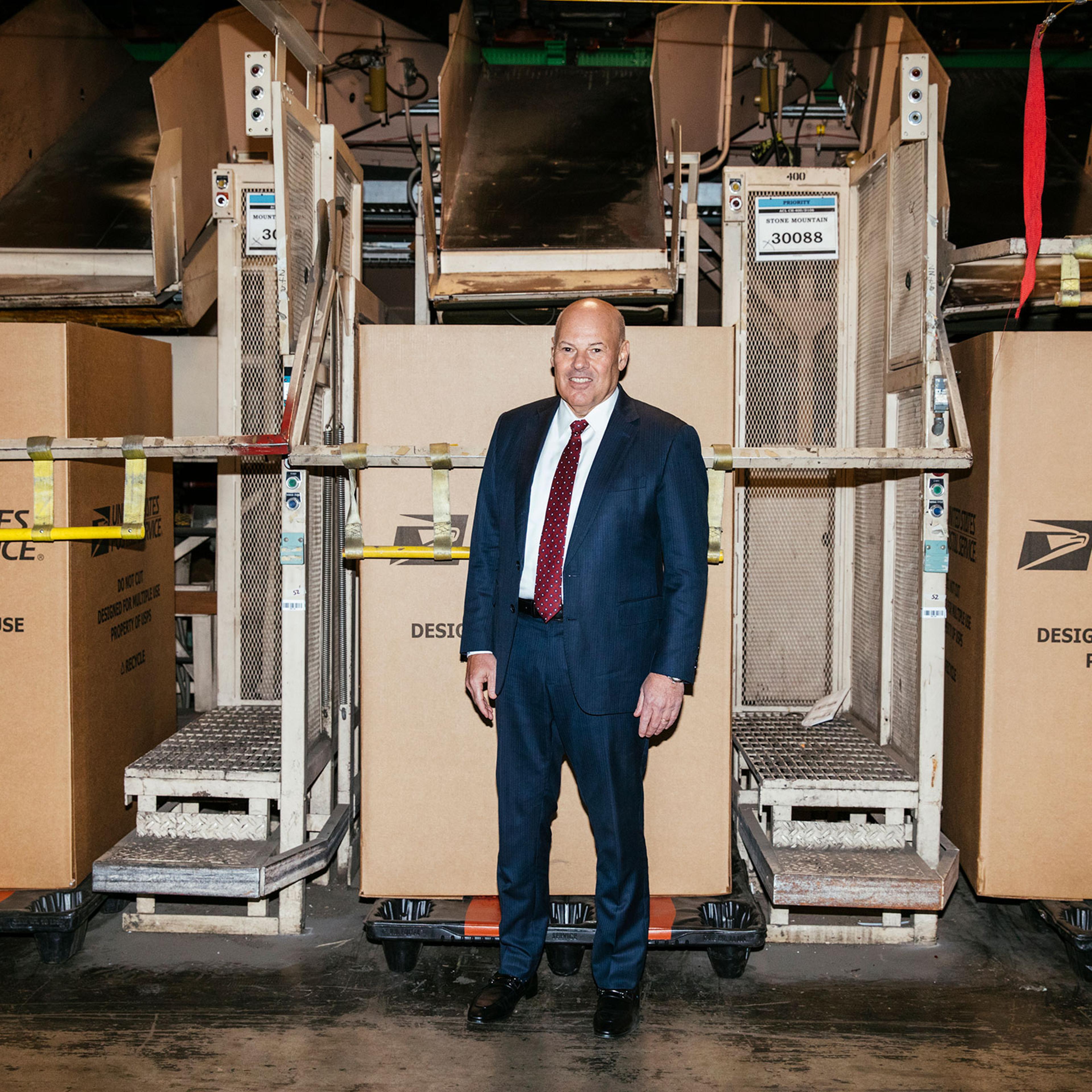 United States Postmaster General Louis DeJoy plans to modernize the outdated postal system. He poses for a portrait in front of a parcel sorting machine at the USPS Atlanta Network Distribution Center in Atlanta, Georgia February 3, 2023. Photo by Kendri