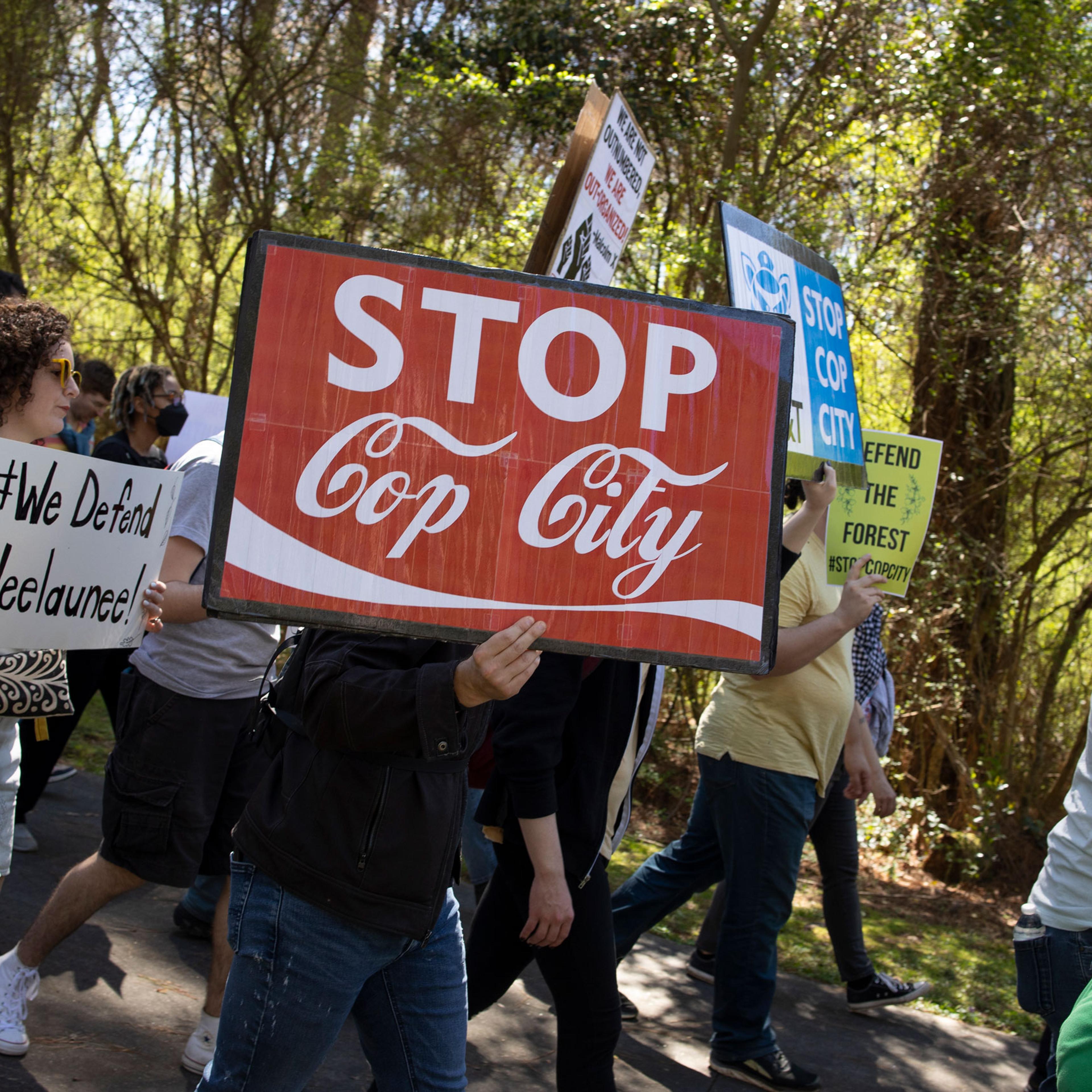 Activists march through a forest holding signs protesting the Cop City development