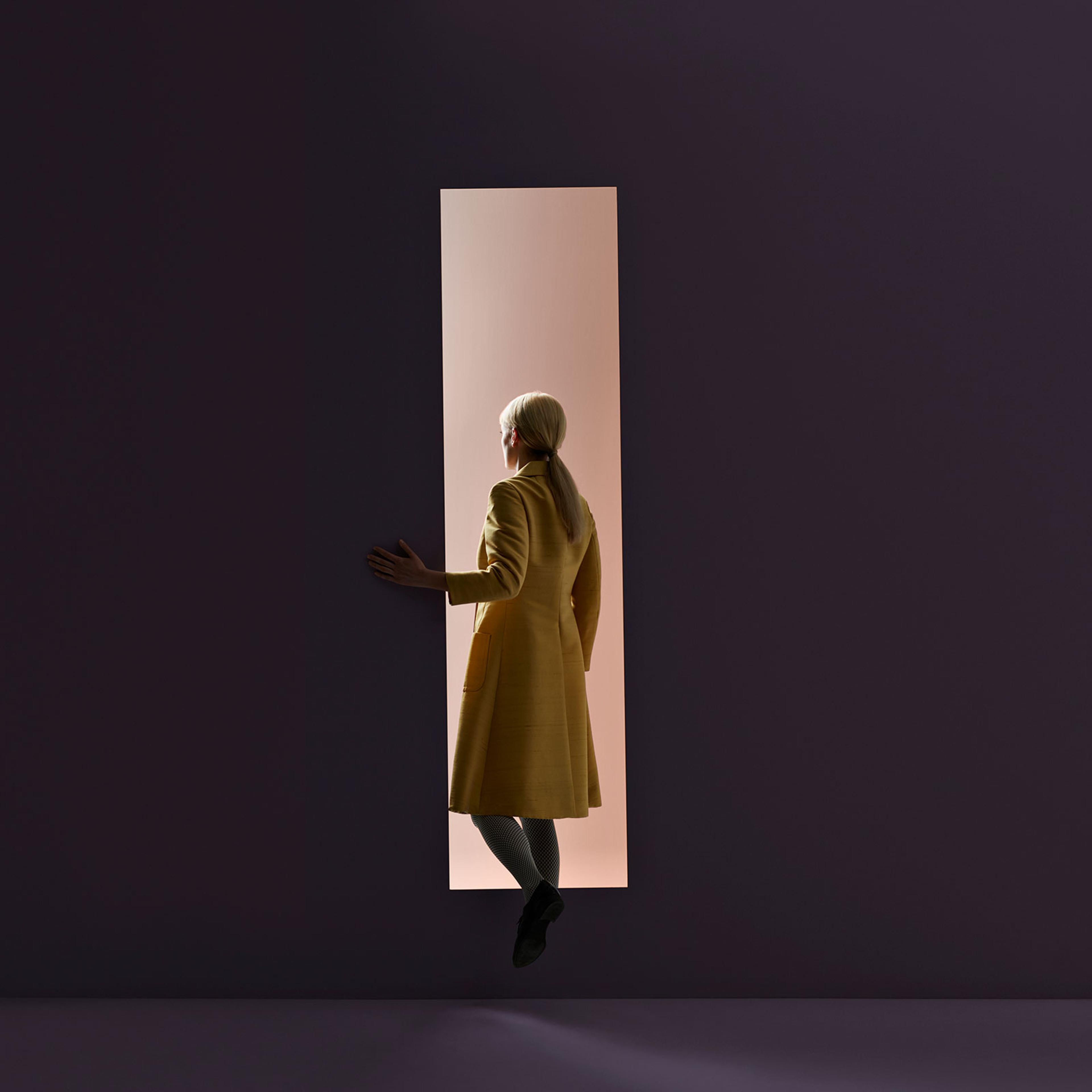 Woman walking into rectangular opening in coloured wall