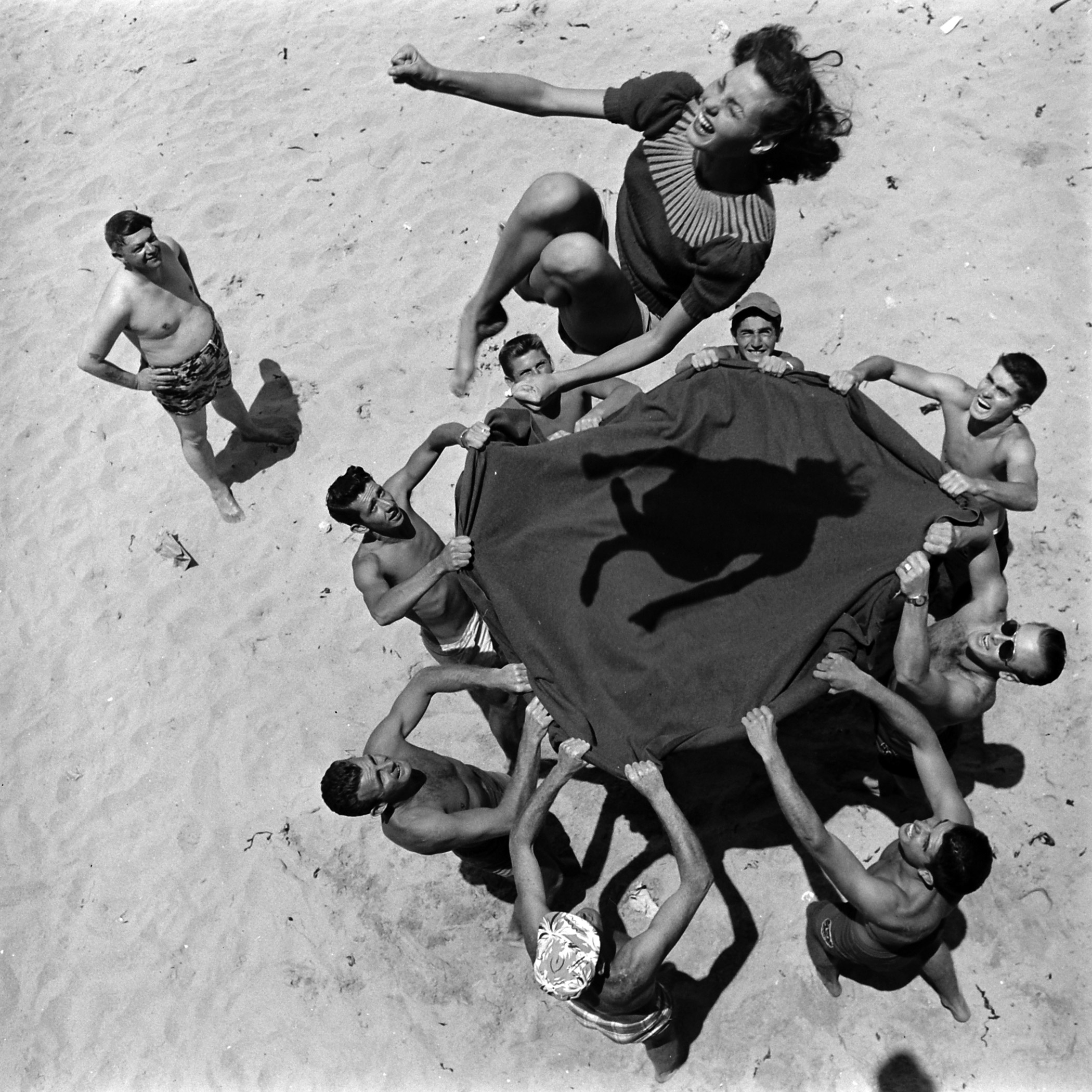 he perils of blanket tossing are happily undergone by pretty Miss Norma Baker with the help of eight husky friends at Hermosa Beach in California.